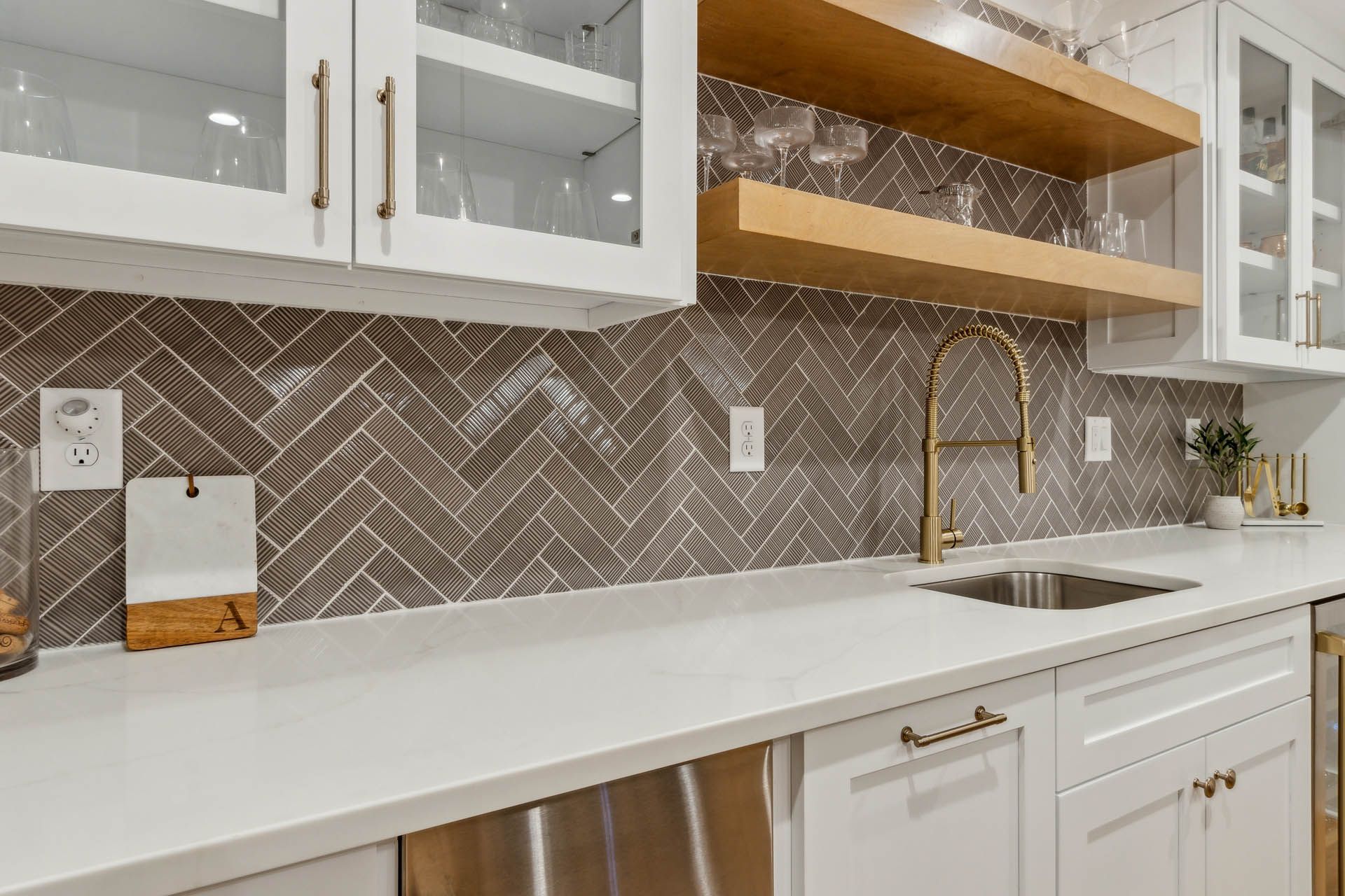 White kitchen with gold accents. Features white cabinets, a white countertop, and a brown tile backsplash.