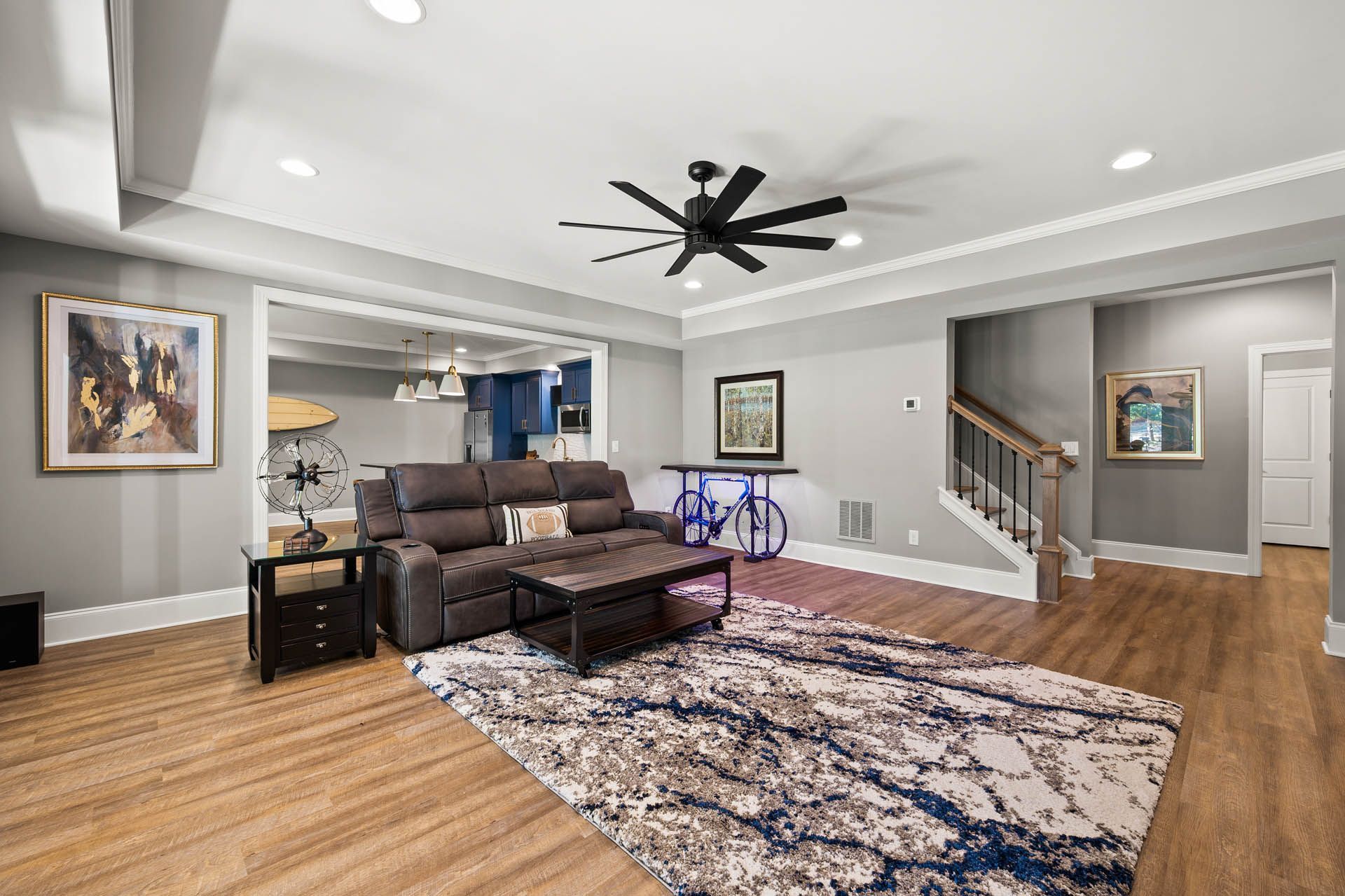 A modern living room with hardwood floors, a gray reclining sofa, and a large rug.  A bicycle is set up behind the sofa.