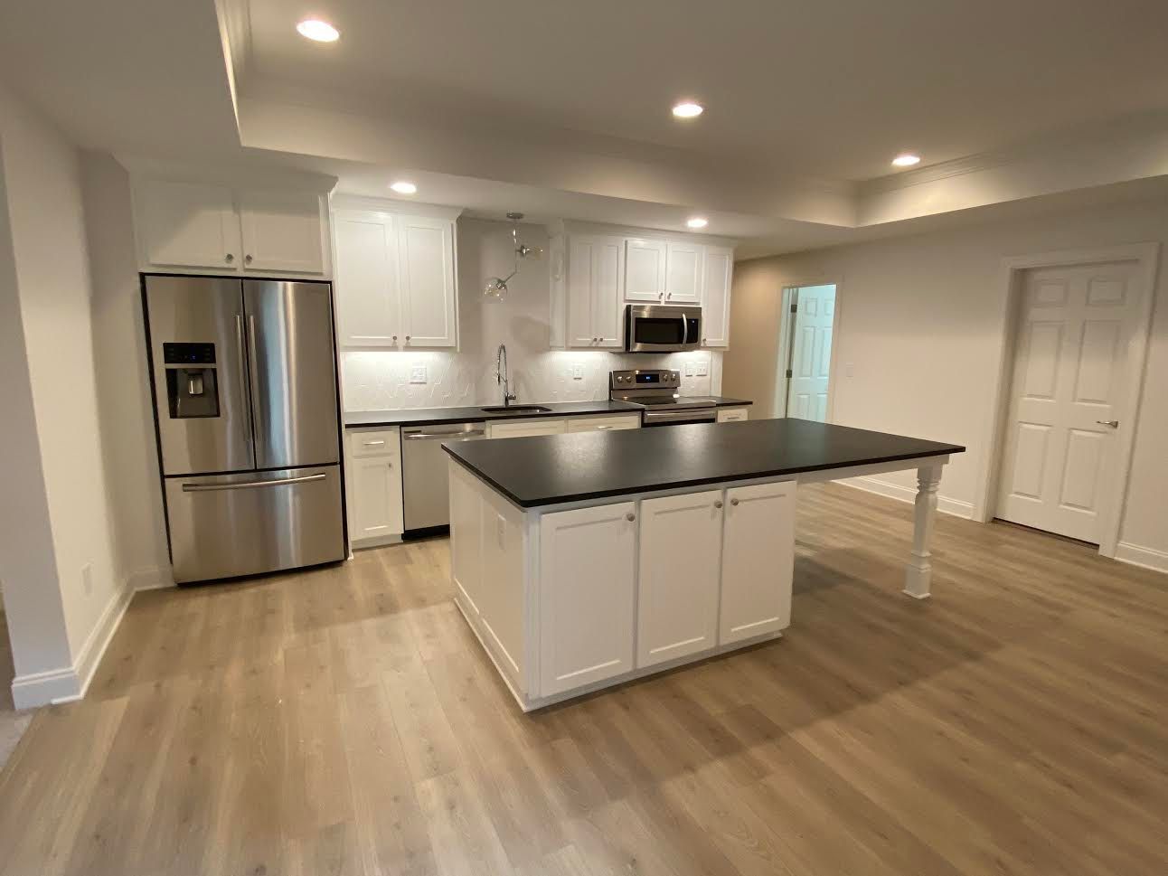 A modern kitchen with white cabinets, stainless steel appliances, and a black countertop island, and light-colored flooring.