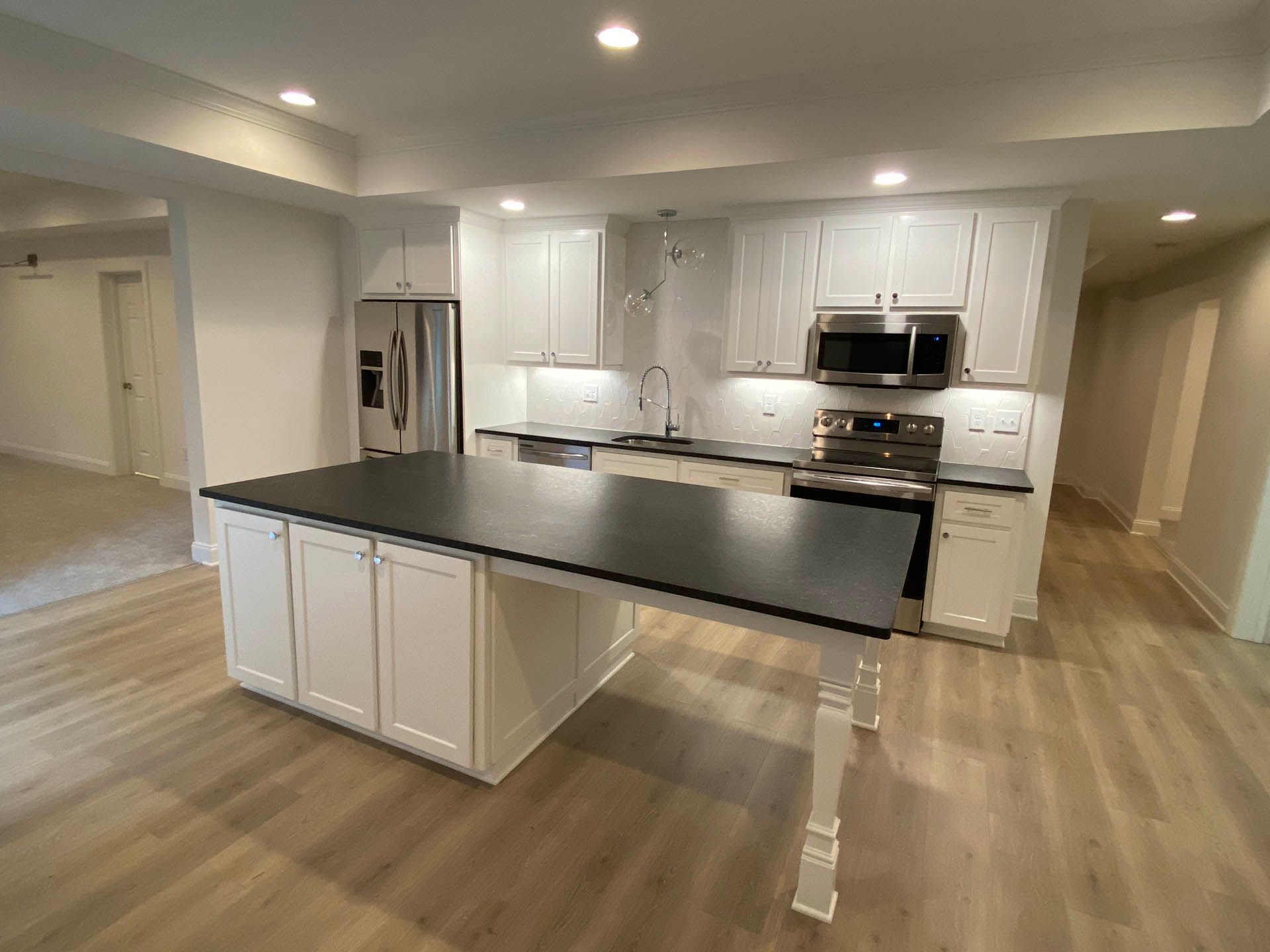 Bright white kitchen with a large black island and stainless steel appliances.  Light wood floors and white cabinets throughout.