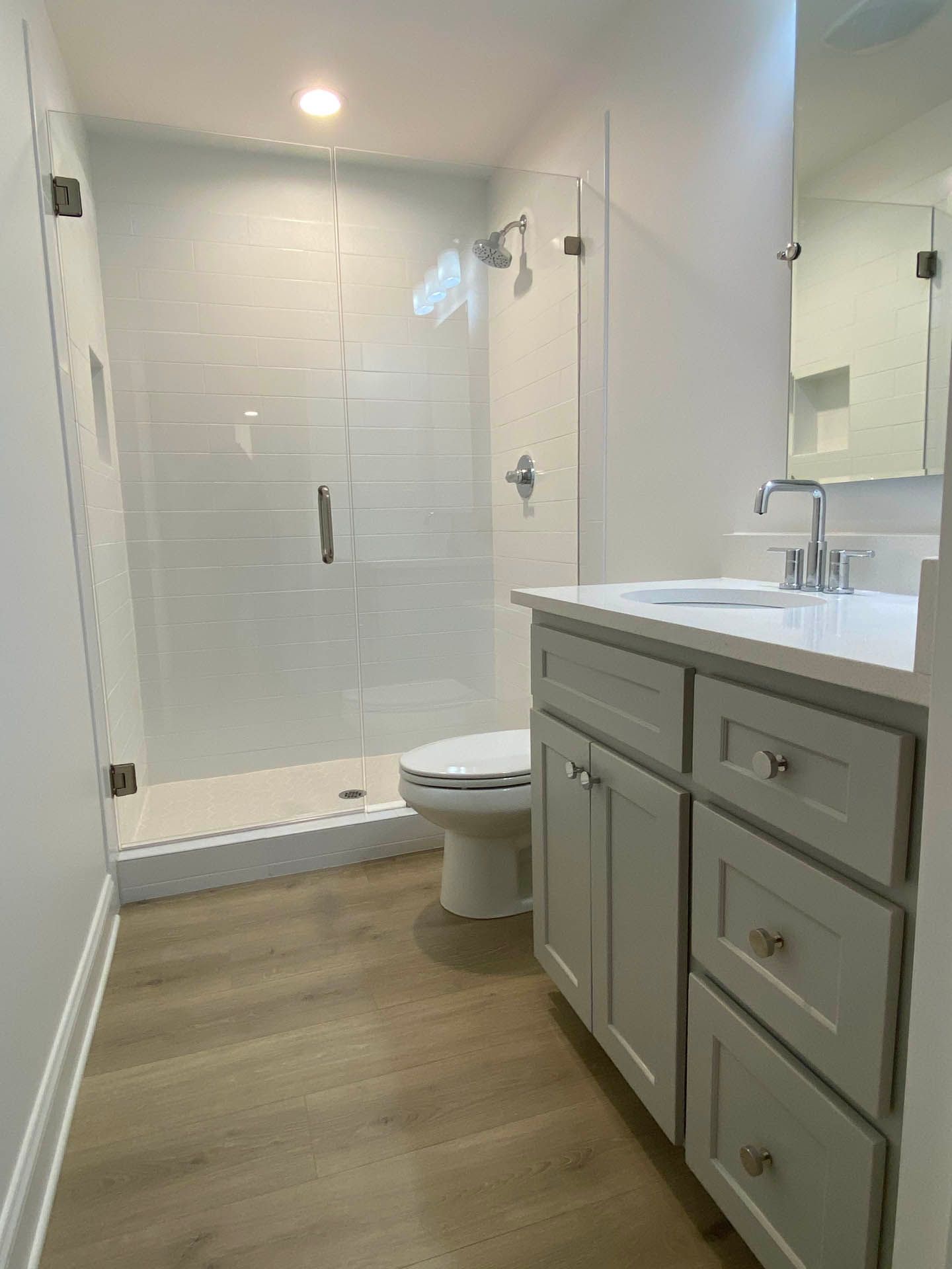 A modern bathroom with a glass shower, white vanity, and light wood-look flooring.