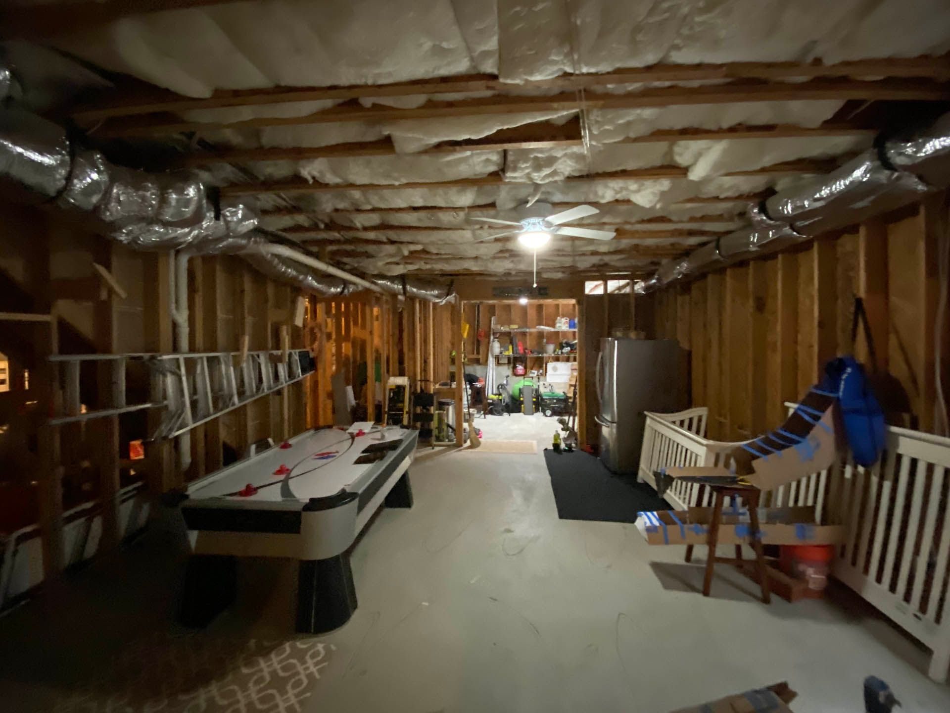 Unfinished basement with a pool table, a crib, and a refrigerator. Framing and exposed ductwork are visible overhead.