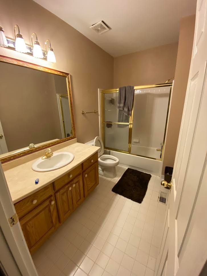 Bathroom with a vanity, toilet, and shower. The walls are beige, and the floor is white tiled.