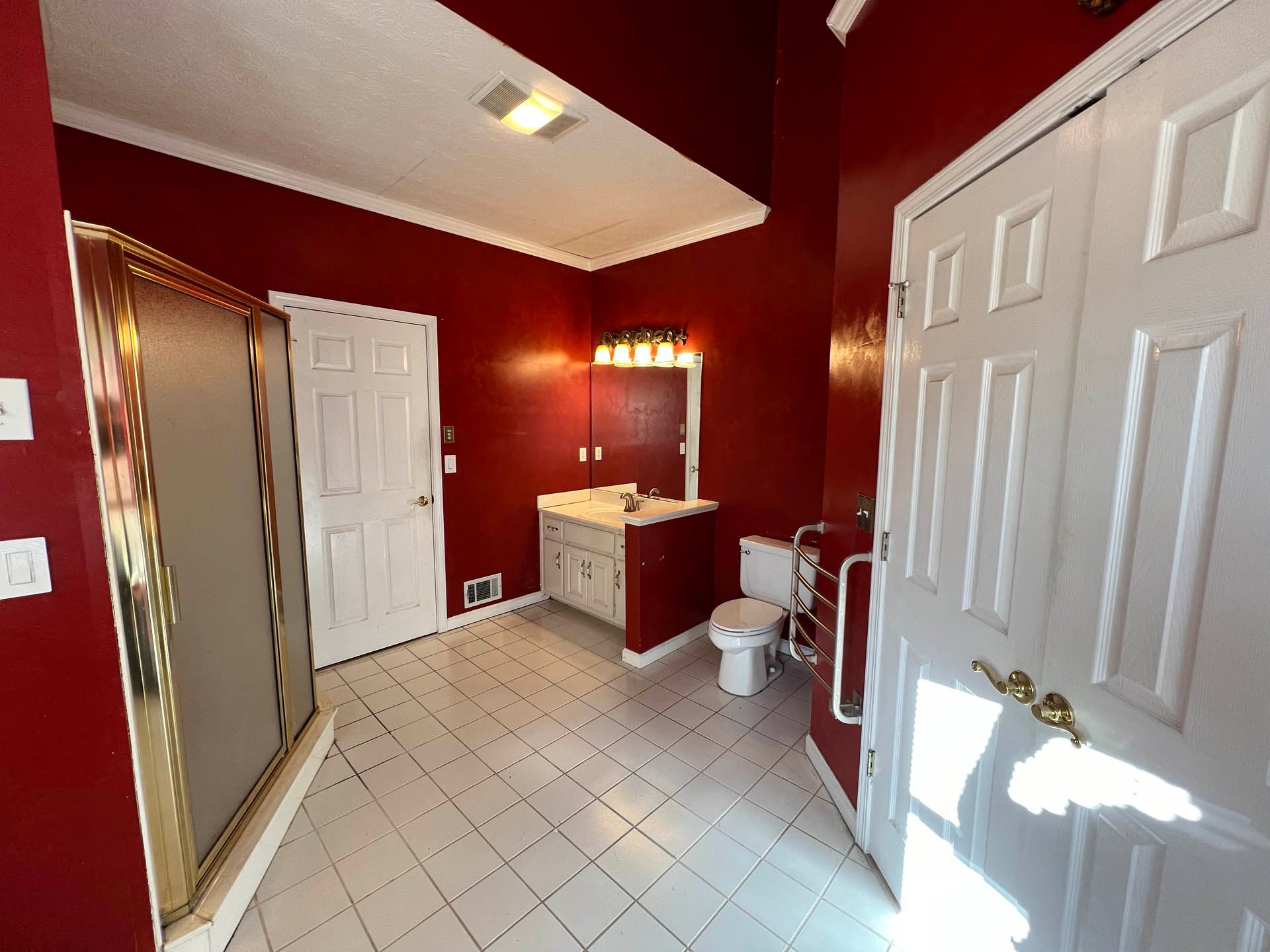 Red-walled bathroom with white trim, white tile floor, and white doors. Includes a vanity, toilet, and shower.