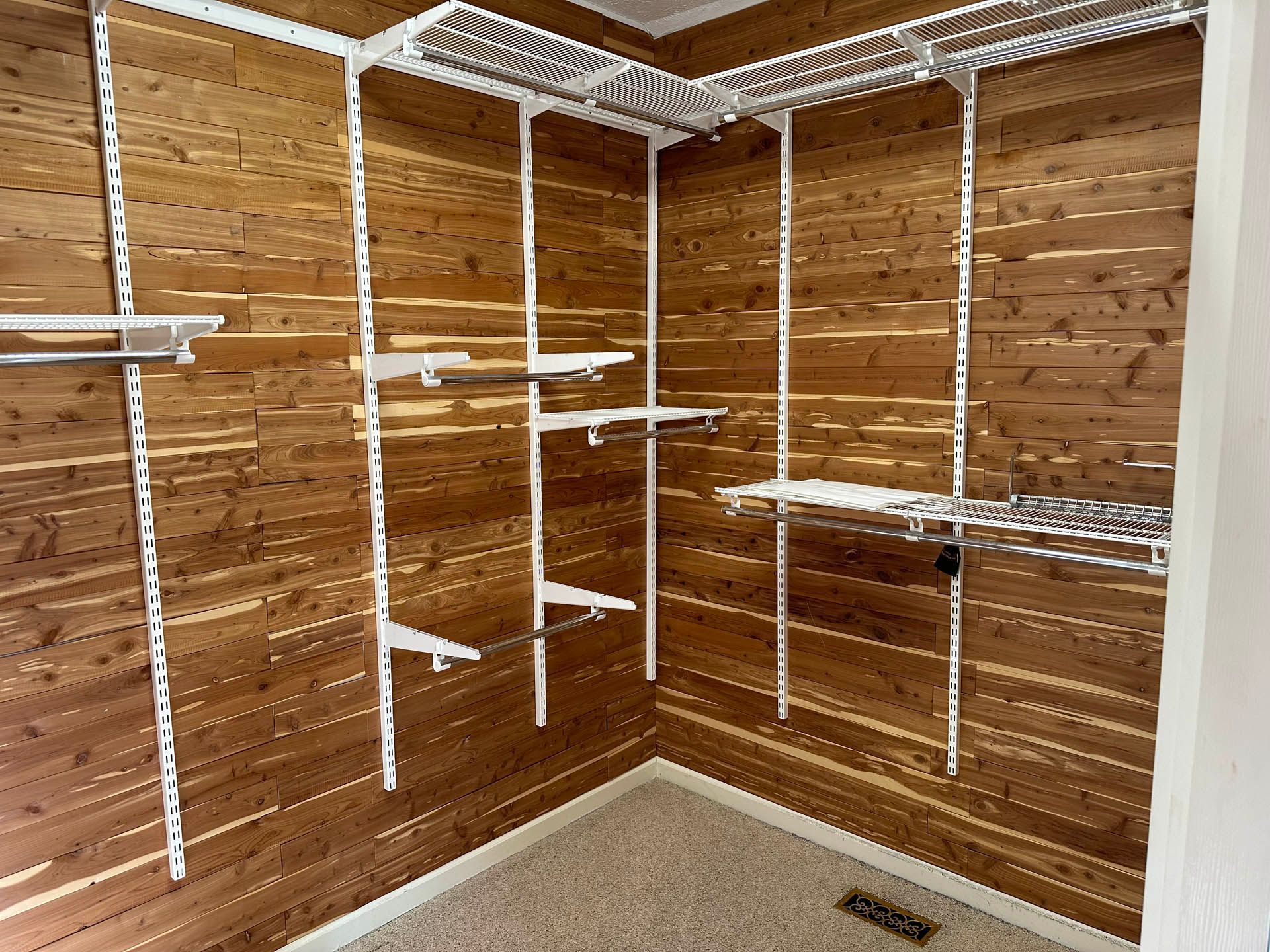 An empty walk-in closet with brown wood paneling and white wire shelving. The closet has a beige carpet floor.