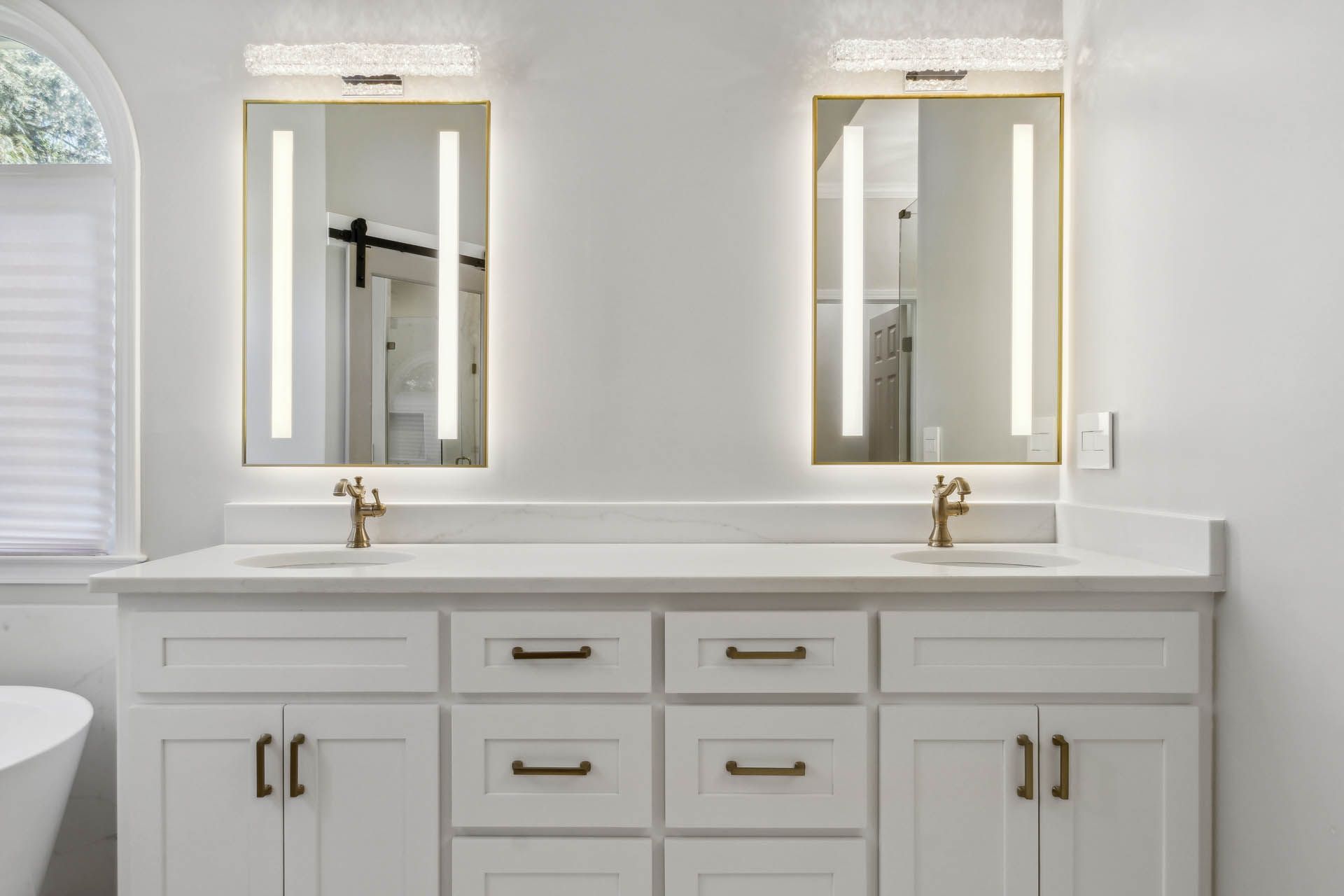 White bathroom vanity with two mirrors and gold accents. The countertop and cabinets are white with brass hardware.