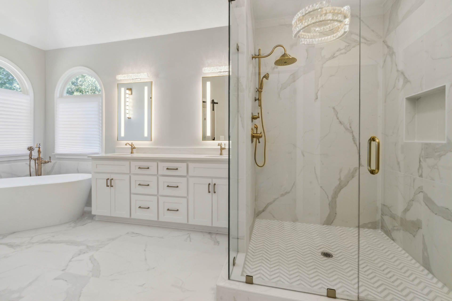 Luxurious white bathroom with a glass shower, gold fixtures, and a freestanding tub.