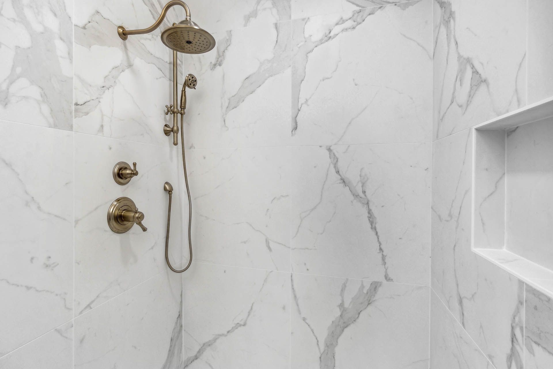 Shower with white marble-patterned walls, bronze fixtures, and a built-in shelf.