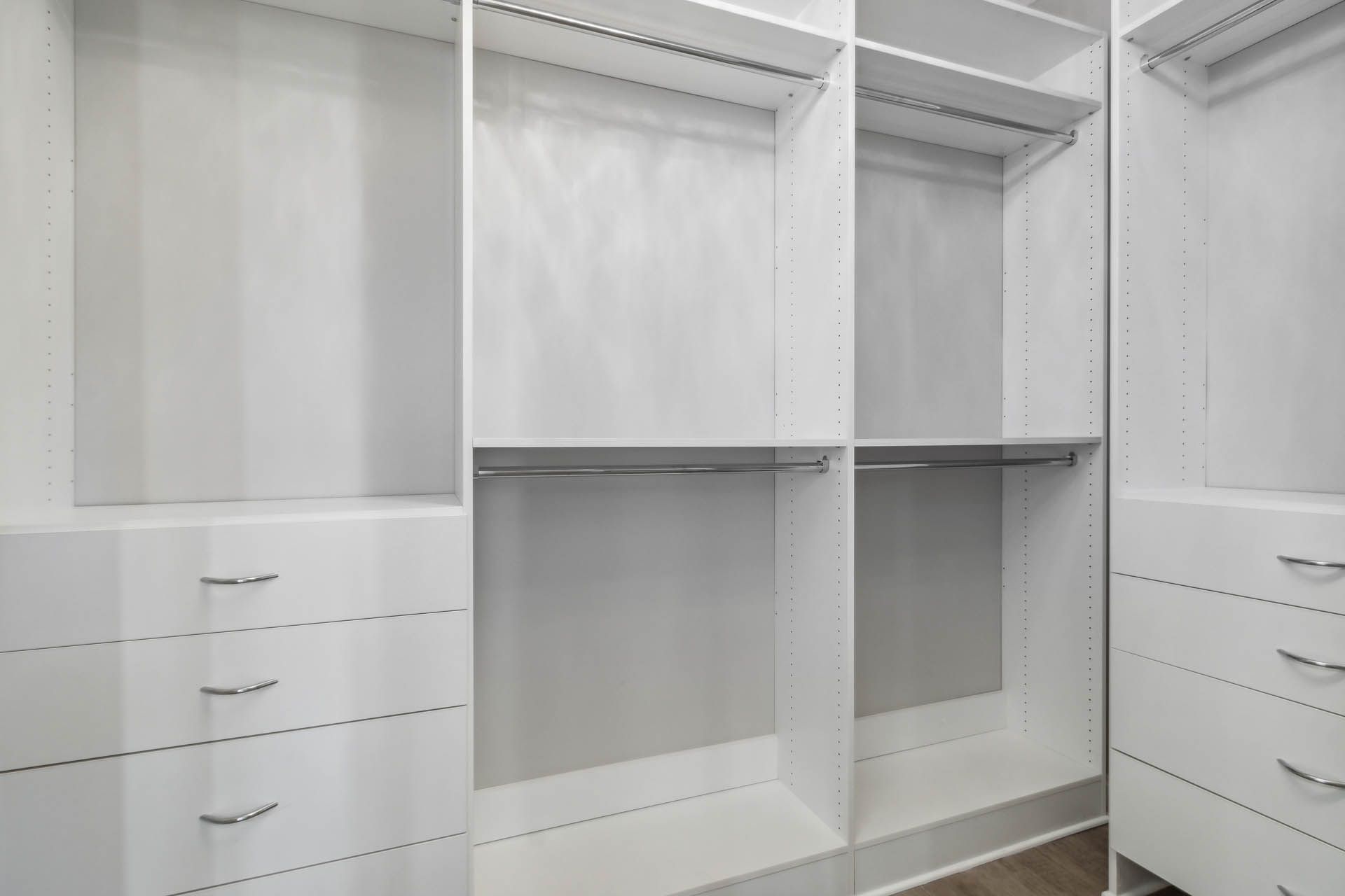 Empty, bright white walk-in closet with drawers, shelves, and hanging rods. Silver drawer pulls are visible.