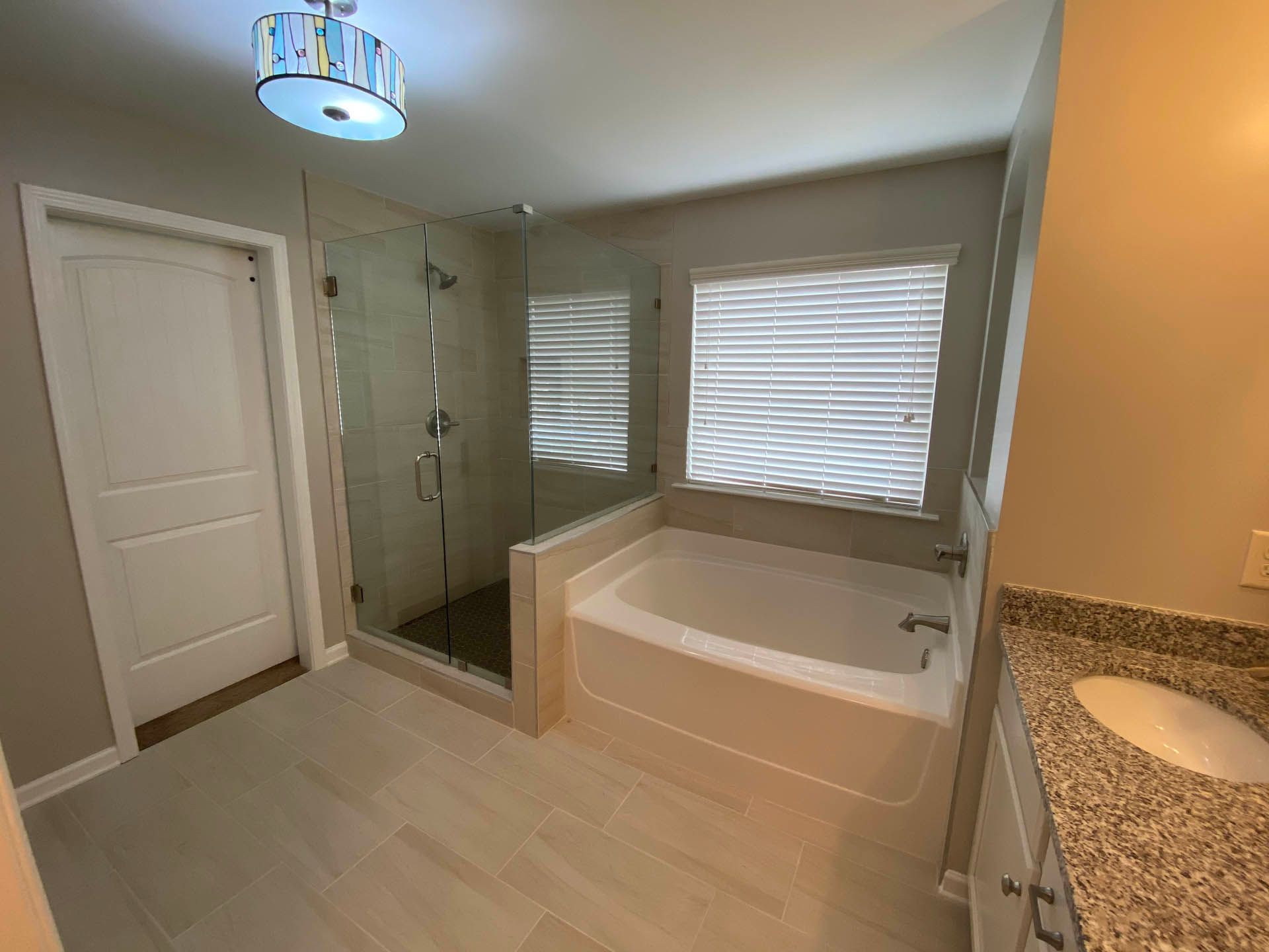 Bathroom with a glass shower, a bathtub, a sink with a granite countertop, and a closed door. The walls are painted light tan.
