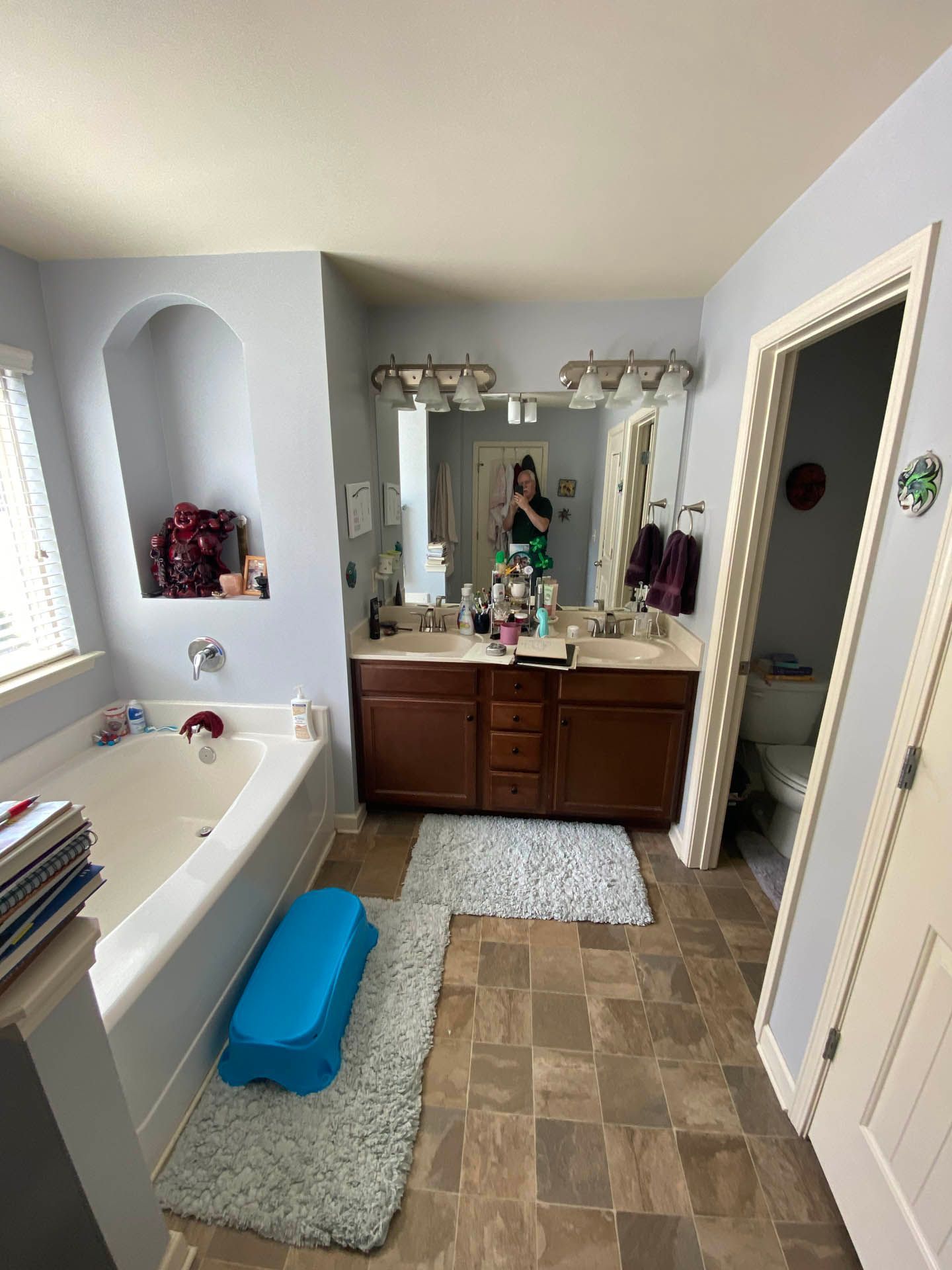 Bathroom with a double vanity, bathtub, and a toilet visible through an open doorway. The walls are light blue, and the cabinets are dark brown.
