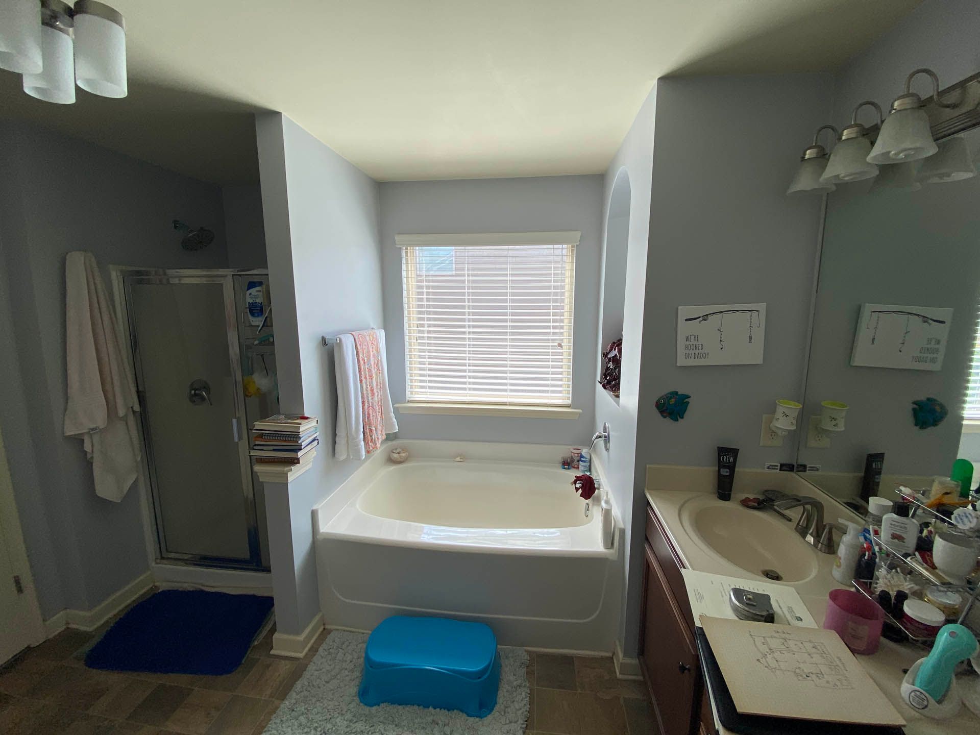 Bathroom with tub, shower, and sink; light blue walls, white tub, and a blue stool.