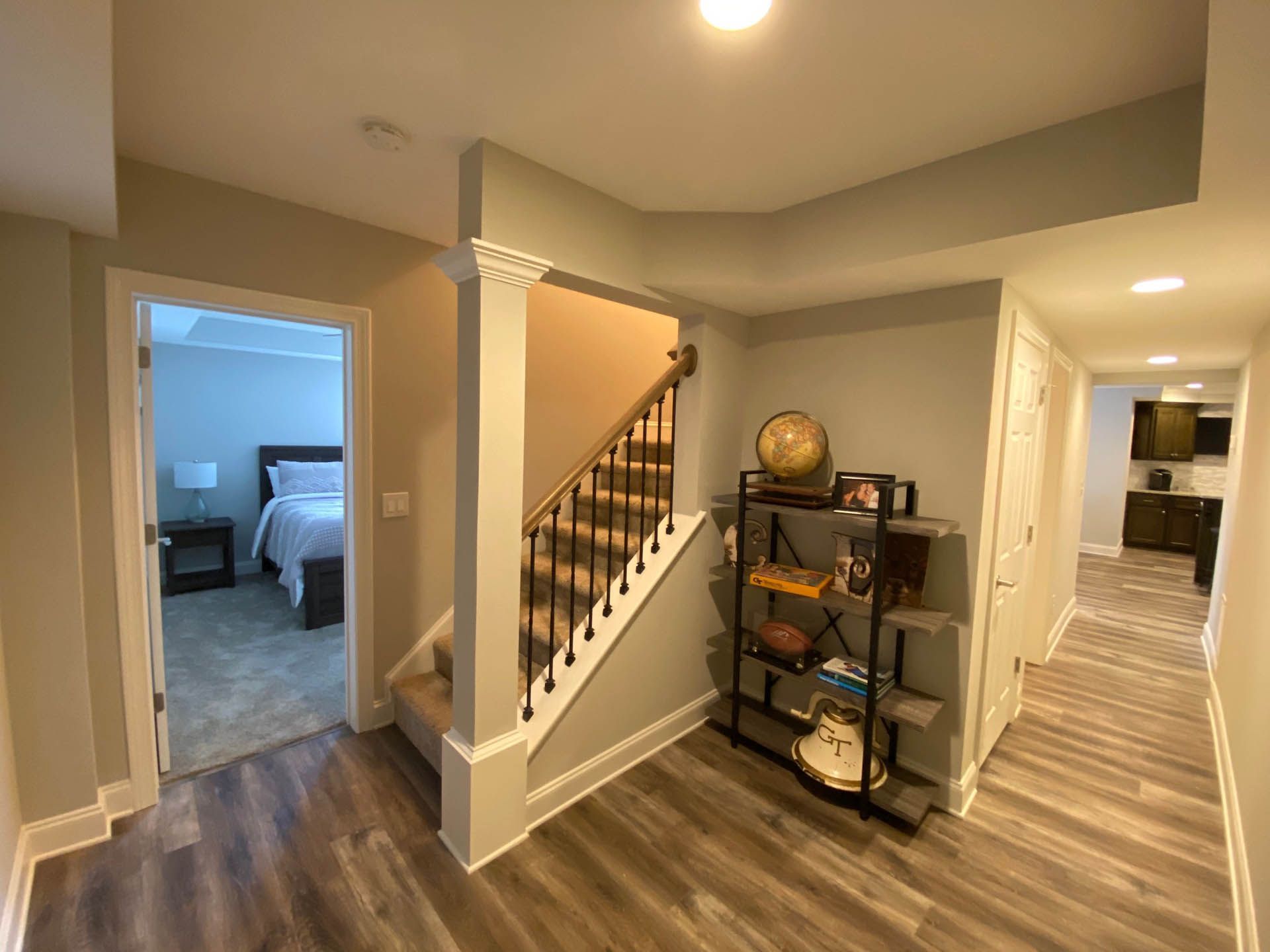 Hallway with stairs, a bedroom door, and a shelving unit. Gray and white walls, brown stairs, and wood-look flooring.