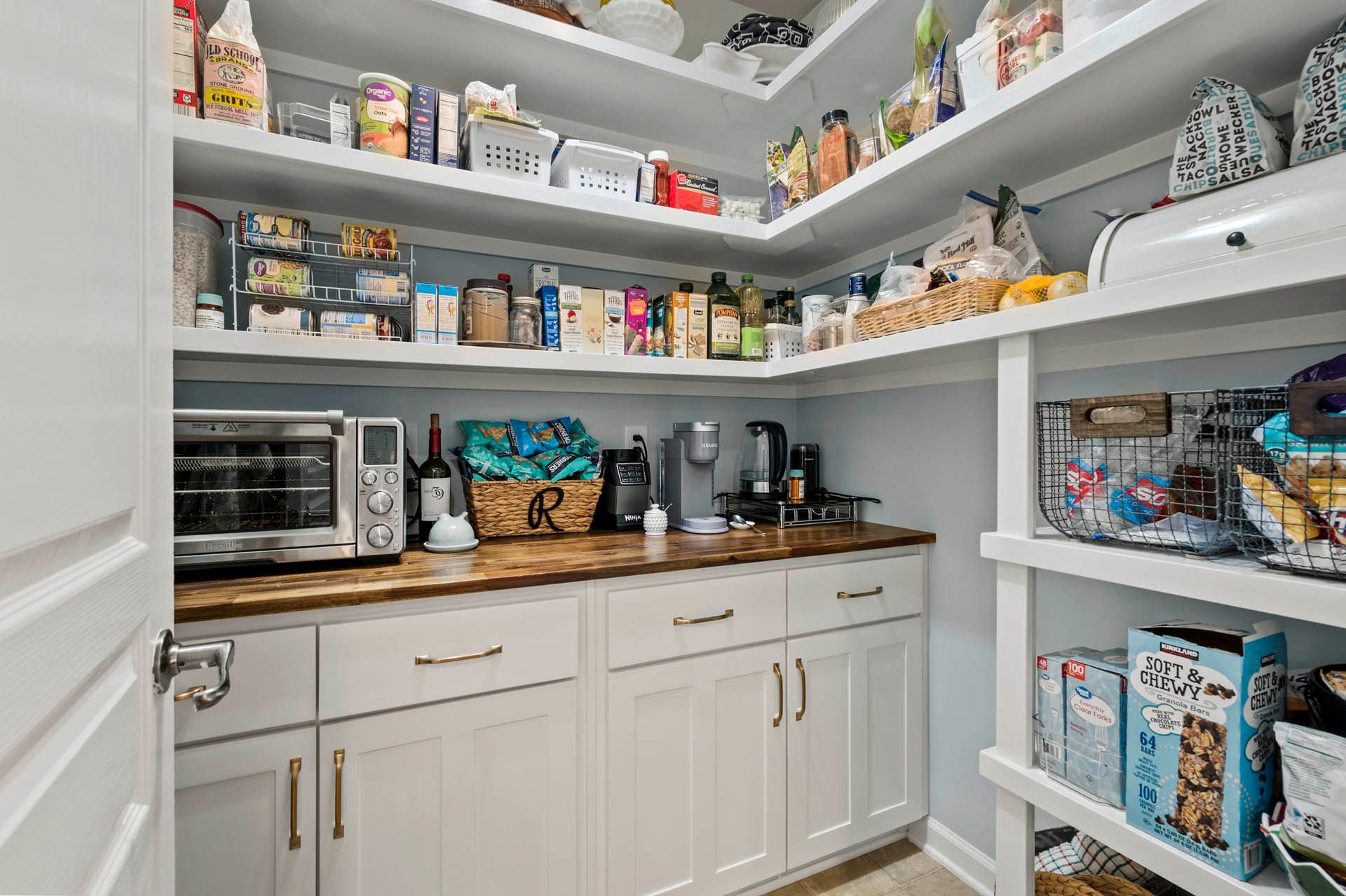 A well-organized pantry with white shelves and cabinets, a countertop, and a toaster oven. Food items are neatly stored on the shelves and counter.