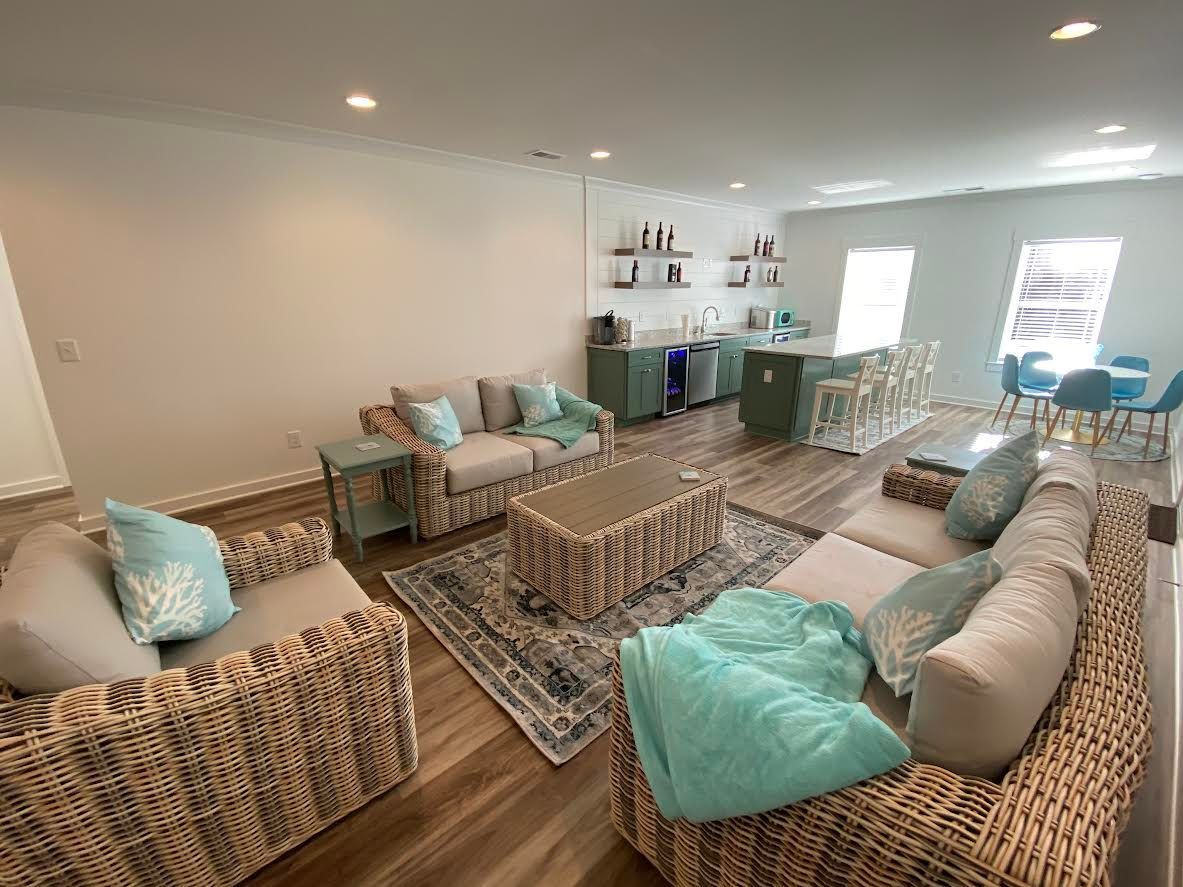 Spacious living room with light-colored wicker furniture, turquoise accents, and a small kitchen area with a breakfast bar.