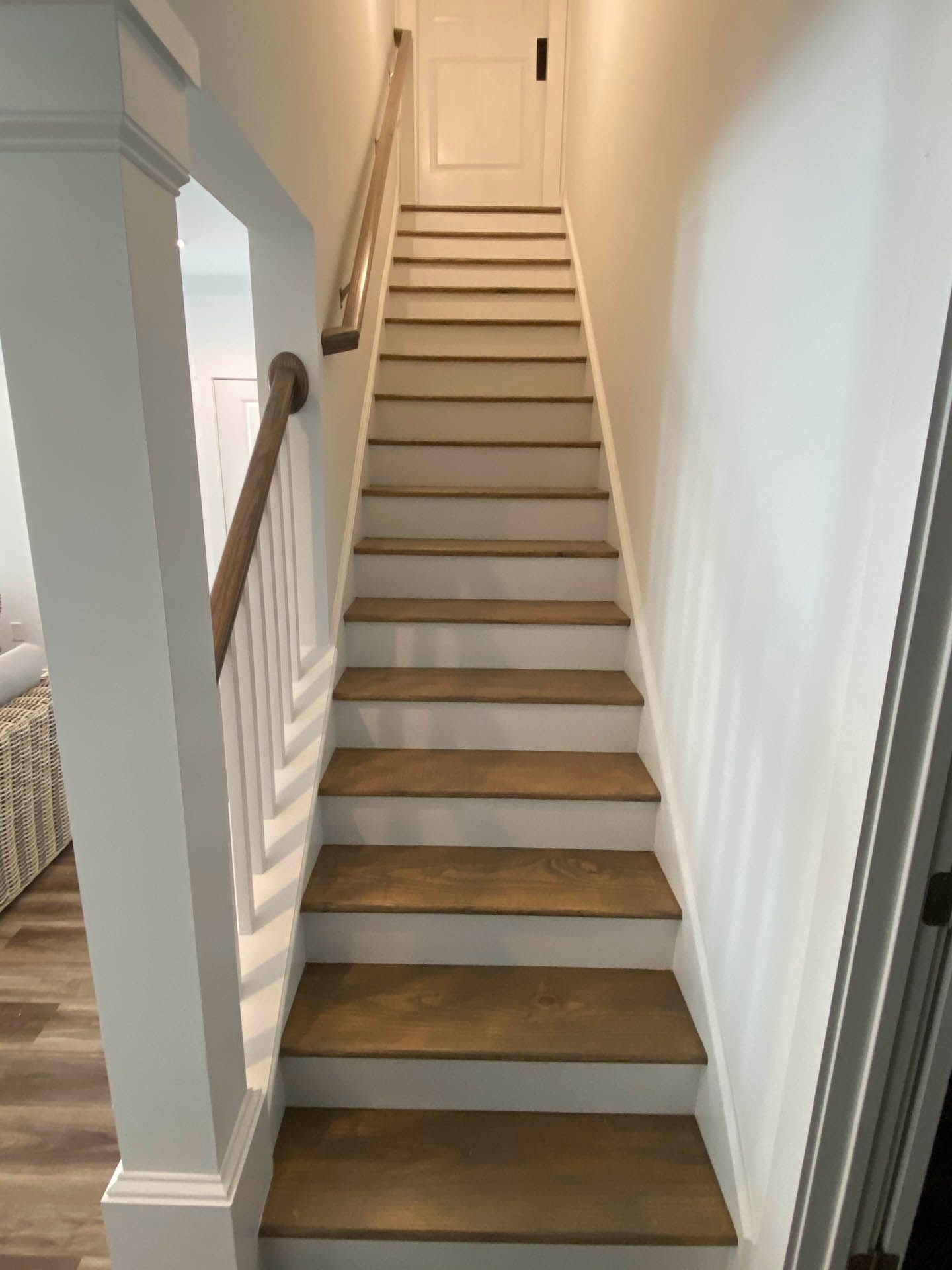Staircase leading upwards with brown treads and white risers, walls, and balusters. A door is at the top.