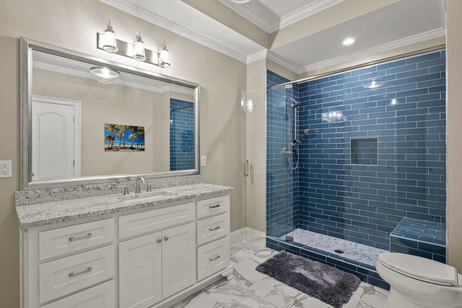 Bathroom with white vanity, blue tiled shower, and large mirror. Gray walls, marble-look flooring, and a decorative blue tiled accent wall.