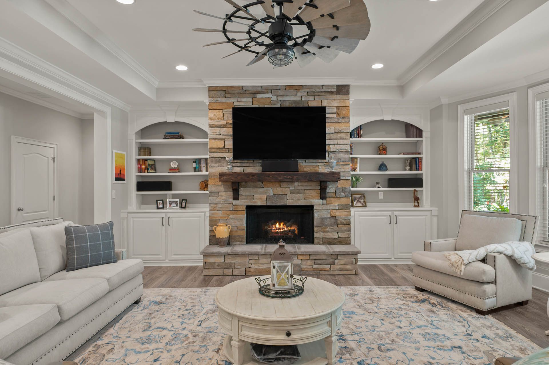 Living room with stone fireplace, built-in bookshelves, and a couch and chair arranged around a coffee table on a patterned rug.