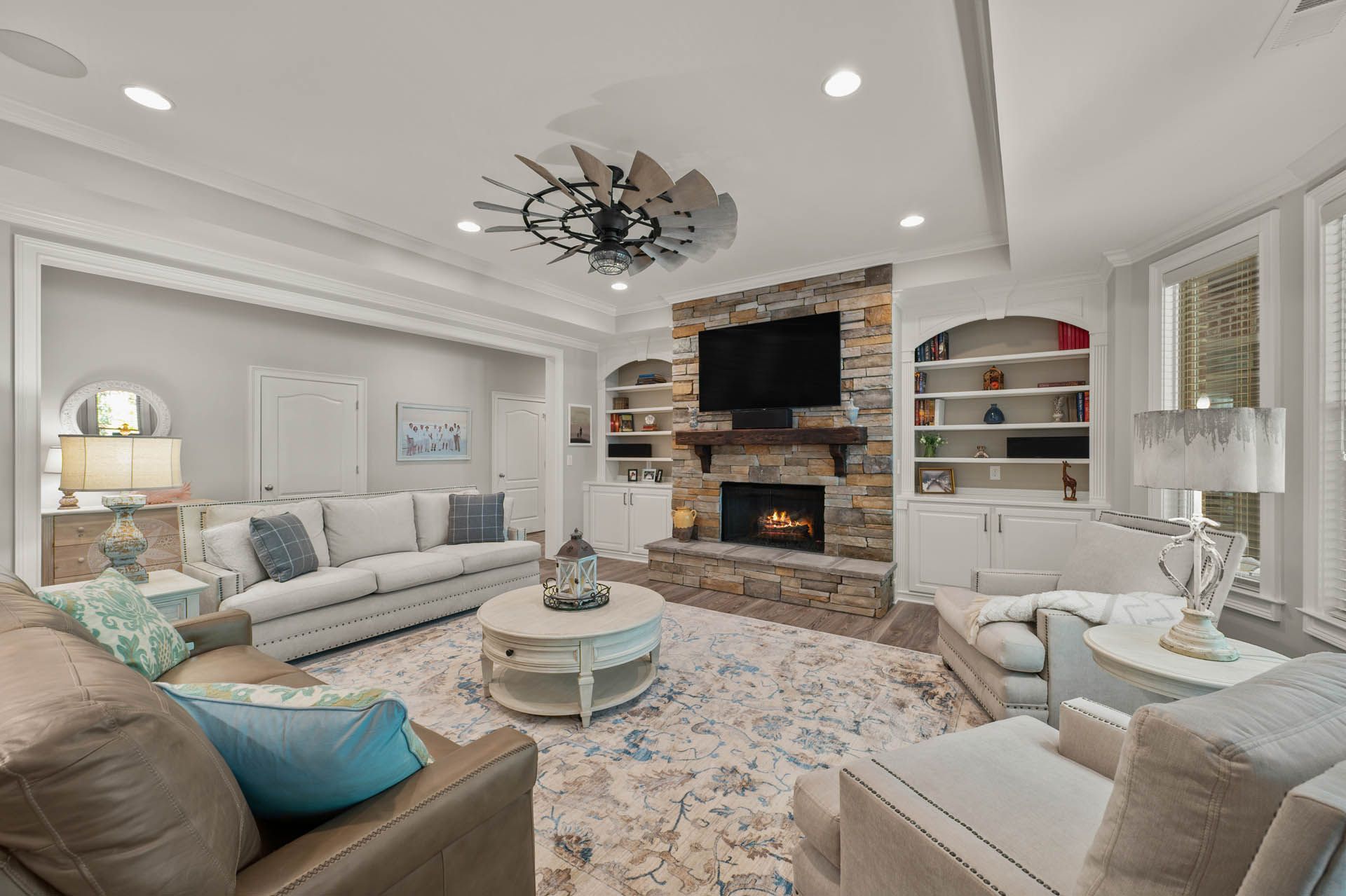 A living room featuring a stone fireplace, built-in bookshelves, white sofas, and a patterned rug.