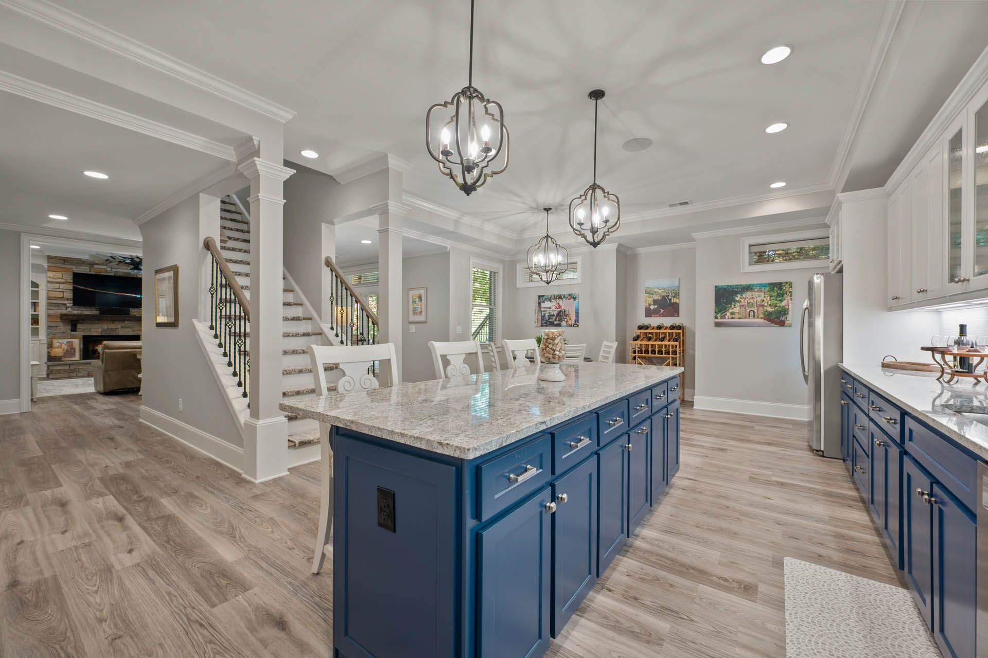 Spacious kitchen with a blue island, white cabinets, and light wood floors; the kitchen is adjacent to a staircase and living area.