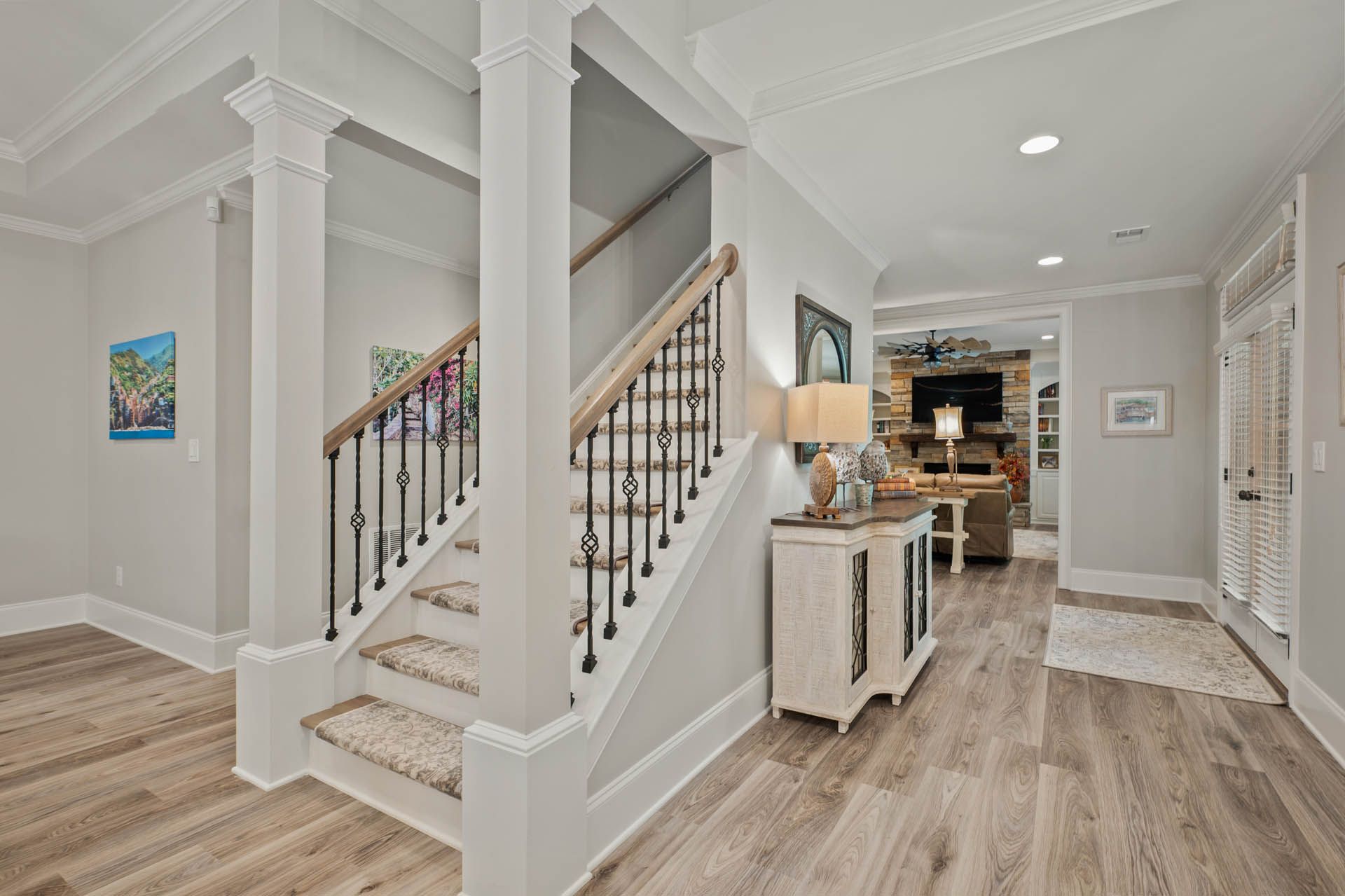 A bright entryway with a staircase and hardwood floors leads to a living room with a fireplace.