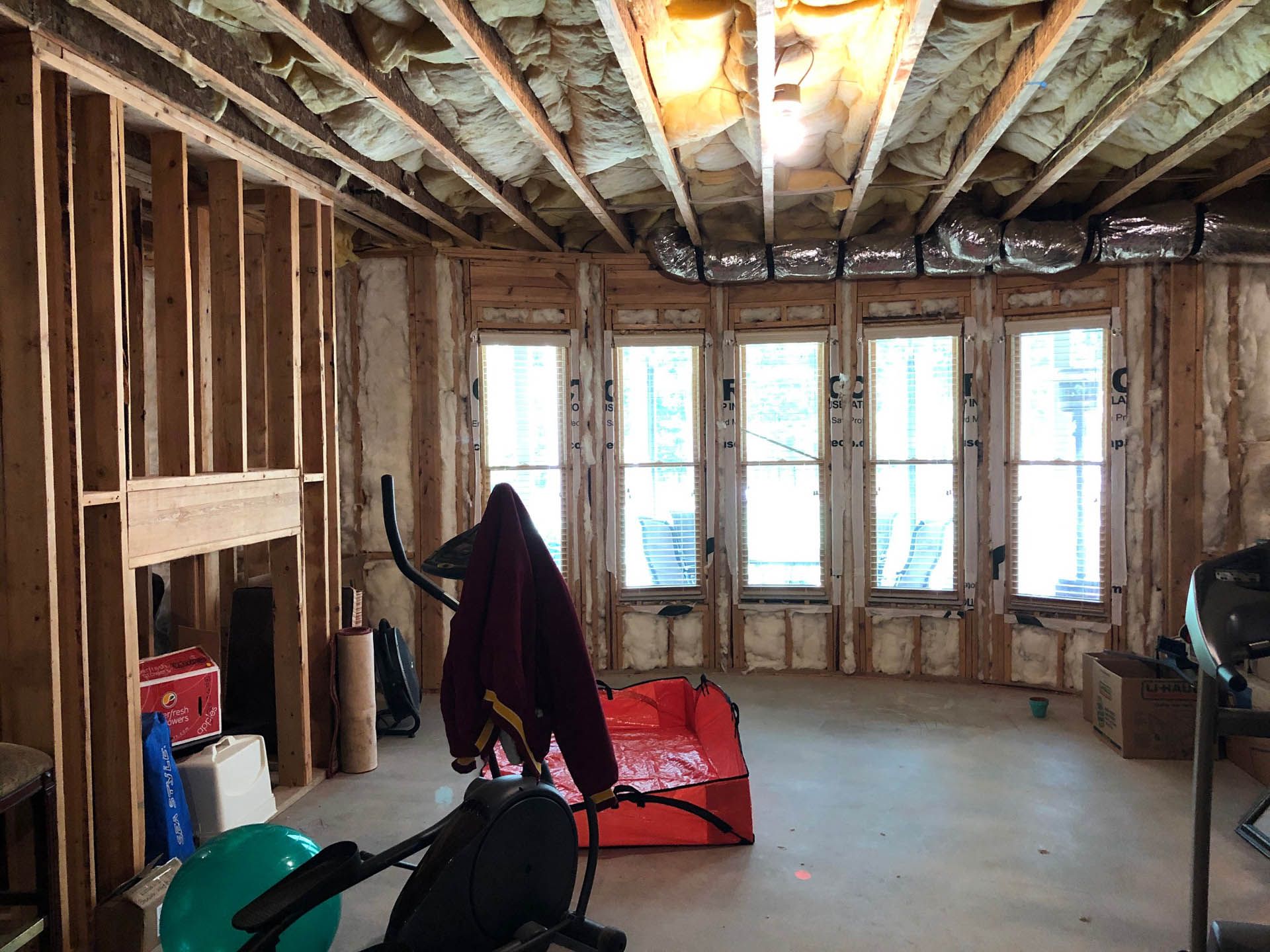 Unfinished room with window bay and framed walls. Exercise equipment, tools, and insulation are visible.