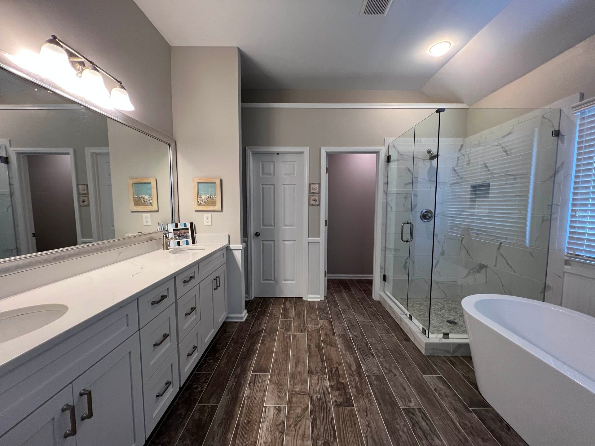 Spacious bathroom with a vanity, large mirror, glass shower, and freestanding tub. Features include wood-look tile flooring and neutral walls.