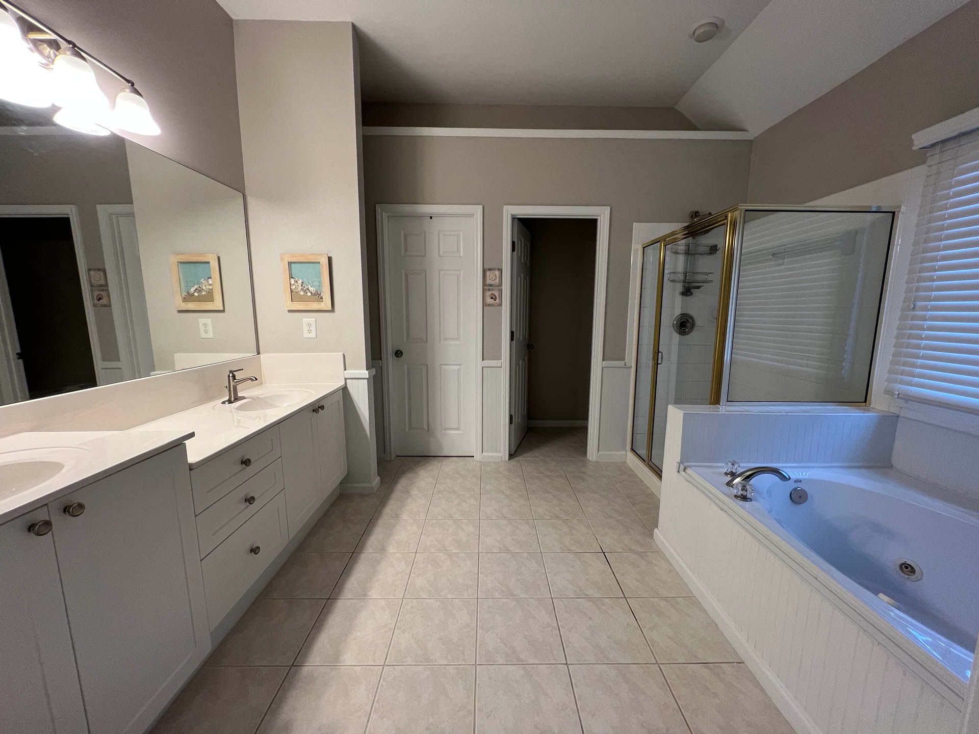 A master bathroom featuring white cabinetry, a soaking tub, a glass shower, and a tiled floor. The walls are painted a light gray.