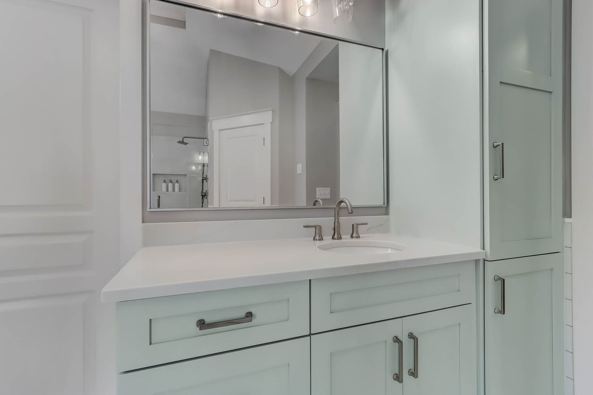 Light blue bathroom vanity with a large mirror, a white countertop, and a tall cabinet.