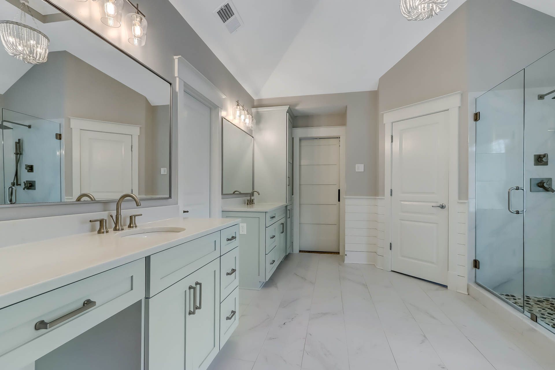 Spacious, bright bathroom with light blue cabinets, white countertops and flooring, and a glass shower.