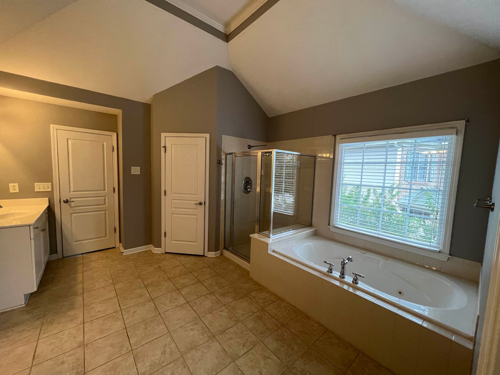 Spacious bathroom with a bathtub, shower, two doors, and a vanity. The walls are gray, and the floor is tiled.