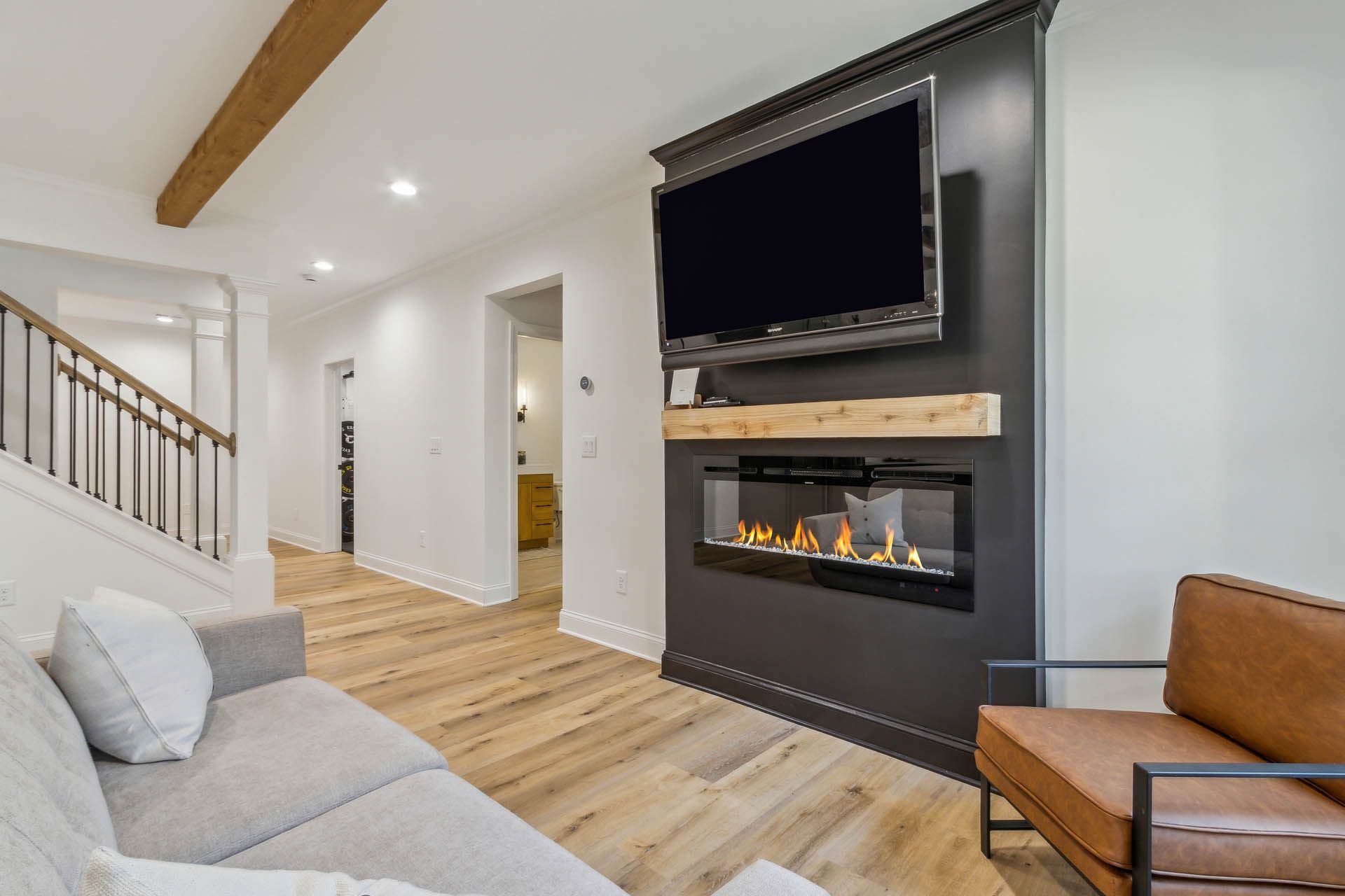 Living room with fireplace, TV, and wooden floor. Gray couch and brown leather chair in front of the fireplace.