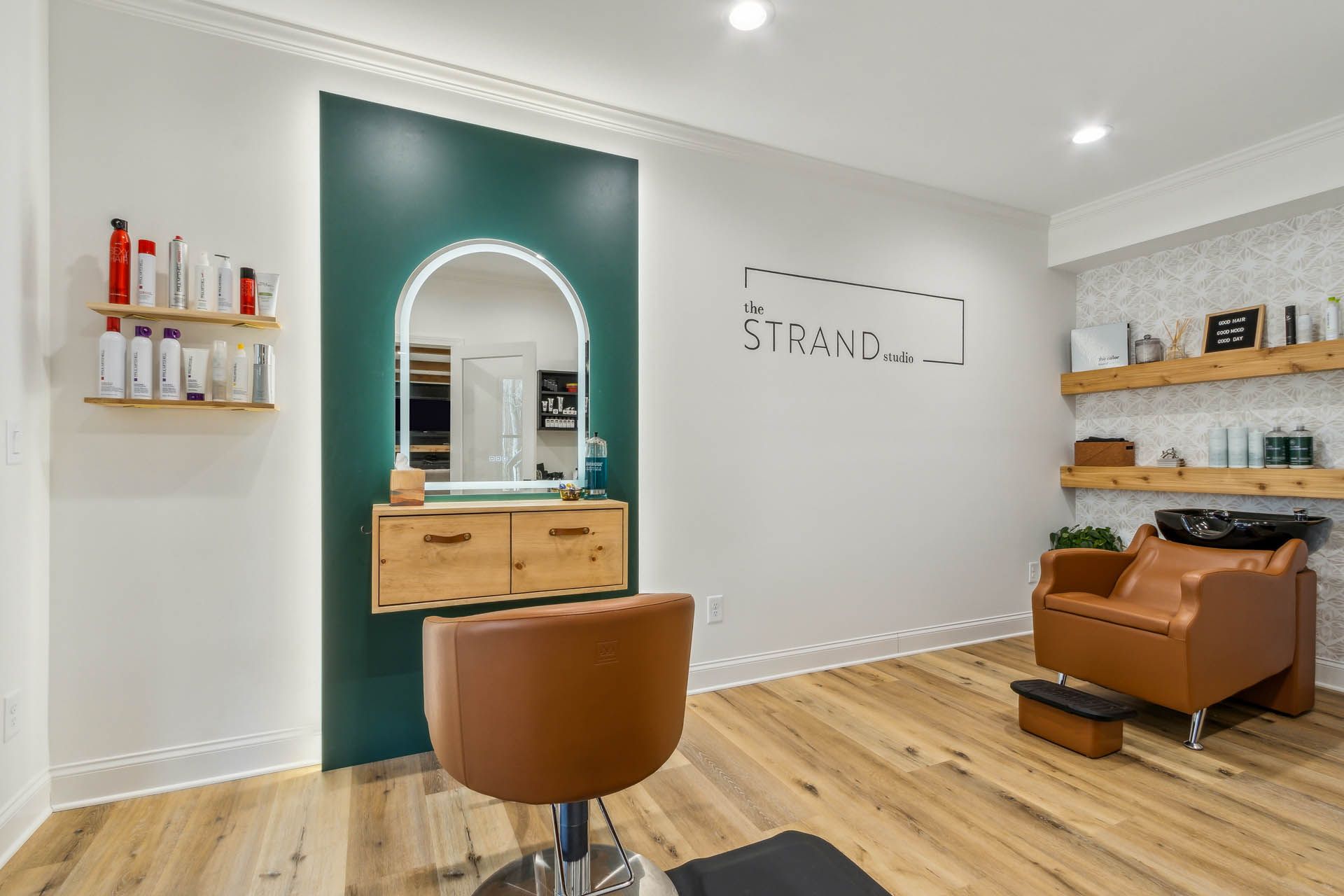 Hair salon interior with a styling station, shampoo chair, wood flooring, and a green accent wall.