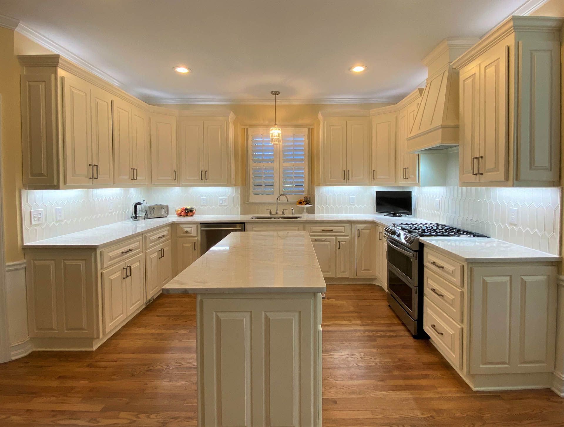 Cream-colored kitchen with an island. Features white countertops, wooden floors, and a stainless steel stove.