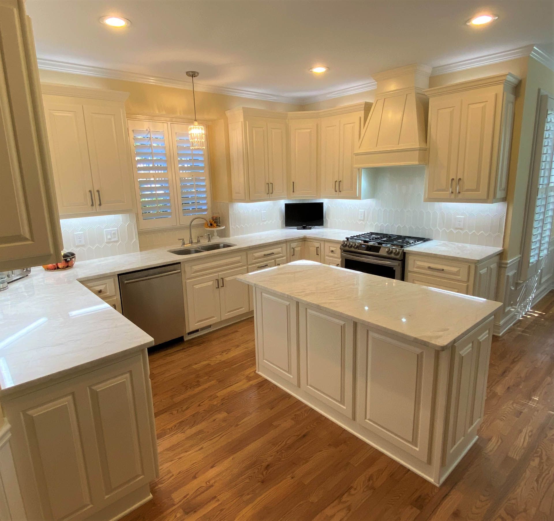 Bright kitchen with cream cabinets, white countertops, and a wooden floor. An island sits in the center.