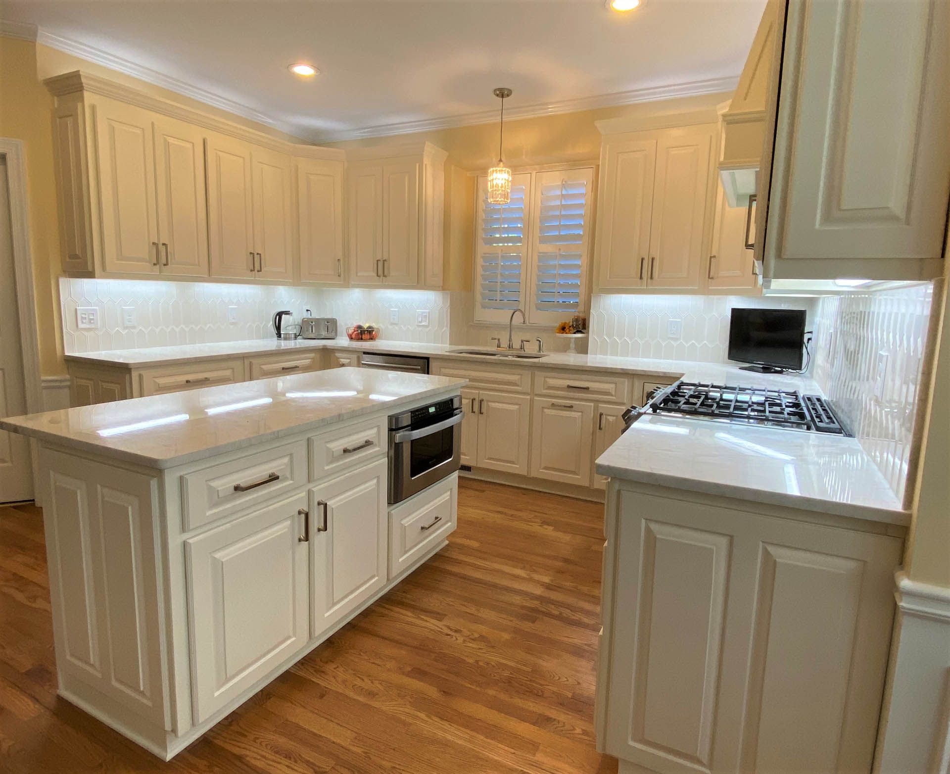 Cream-colored kitchen with a large island and white countertops. Light wood floors and overhead lighting.