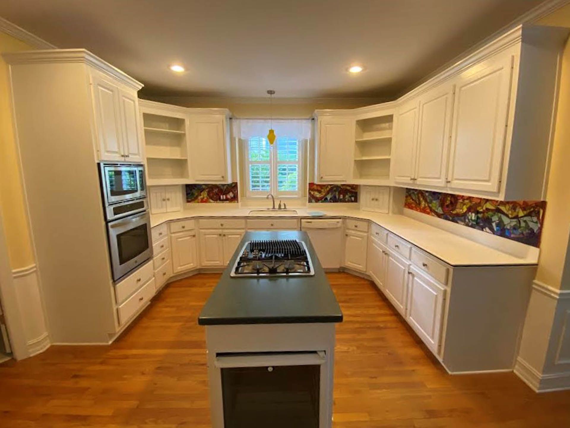 White kitchen with a curved counter, island stove, and colorful backsplash. The setting is brightly lit with hardwood floors.