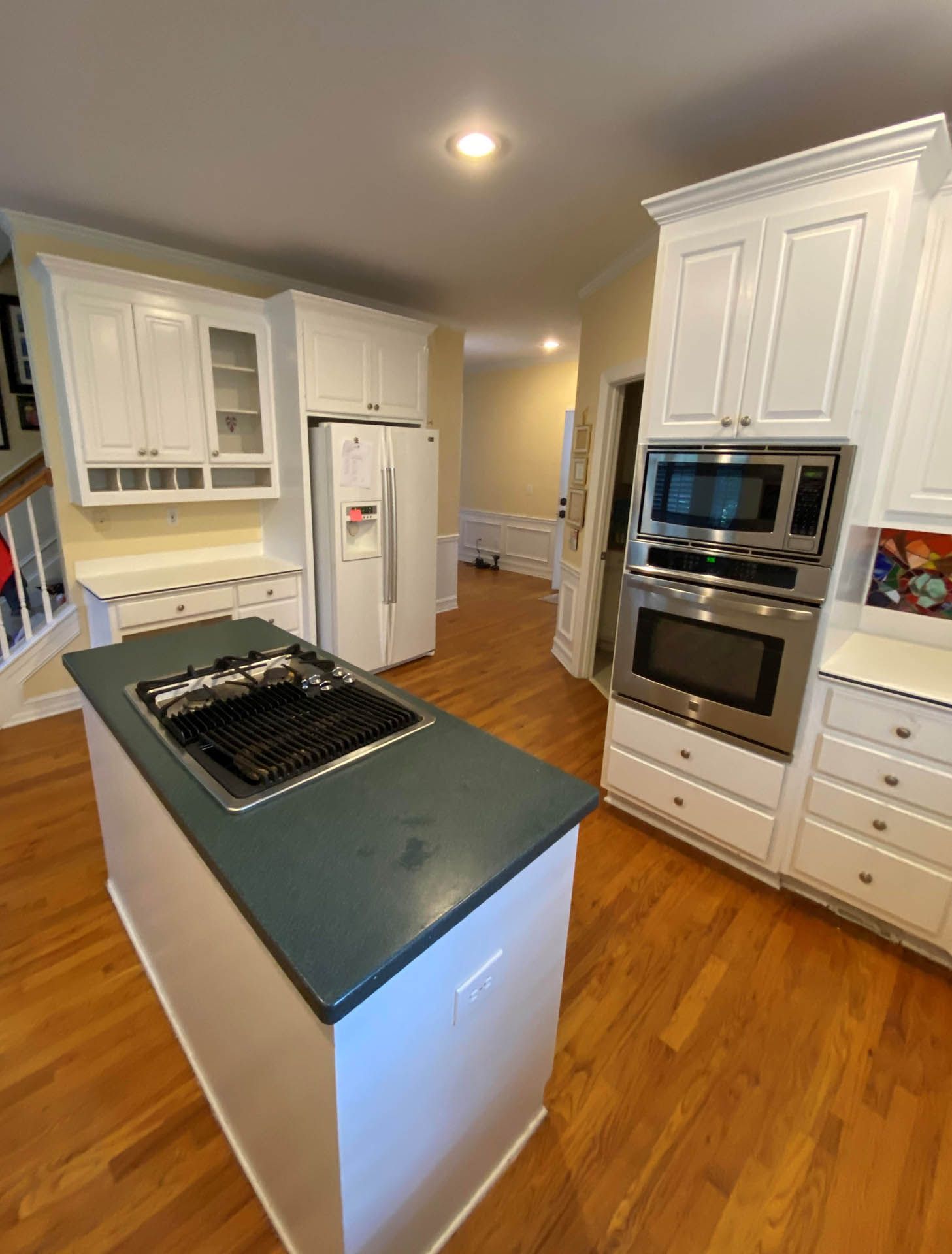 A kitchen with white cabinets, a central island with a stovetop, and stainless steel appliances. Hardwood floors and yellow walls.