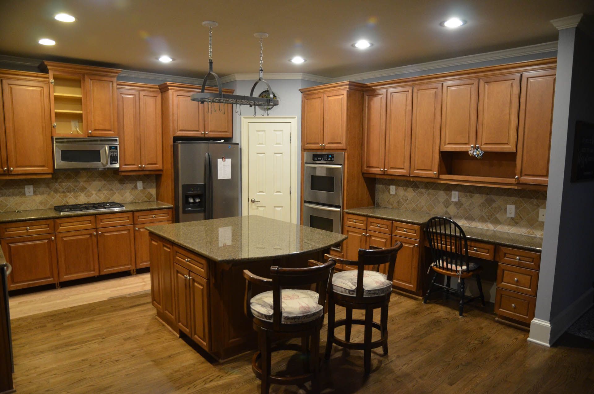 Spacious kitchen with wooden cabinets, granite countertops, and an island with two bar stools. A stainless steel refrigerator and built-in oven are also present.
