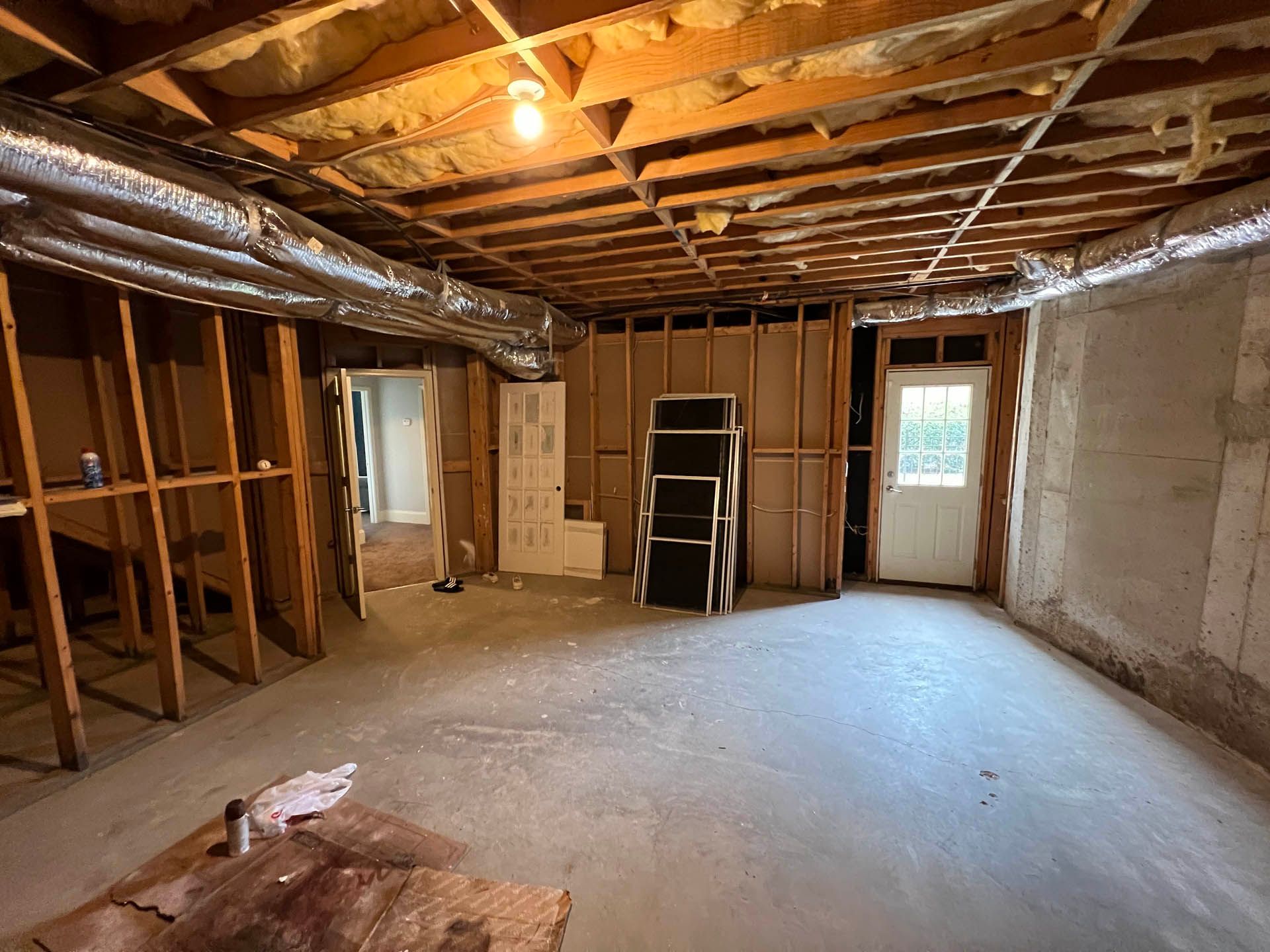 Basement interior with exposed framing. Concrete floor, unfinished walls, and open ceiling with insulation. Two doorways and a ladder.
