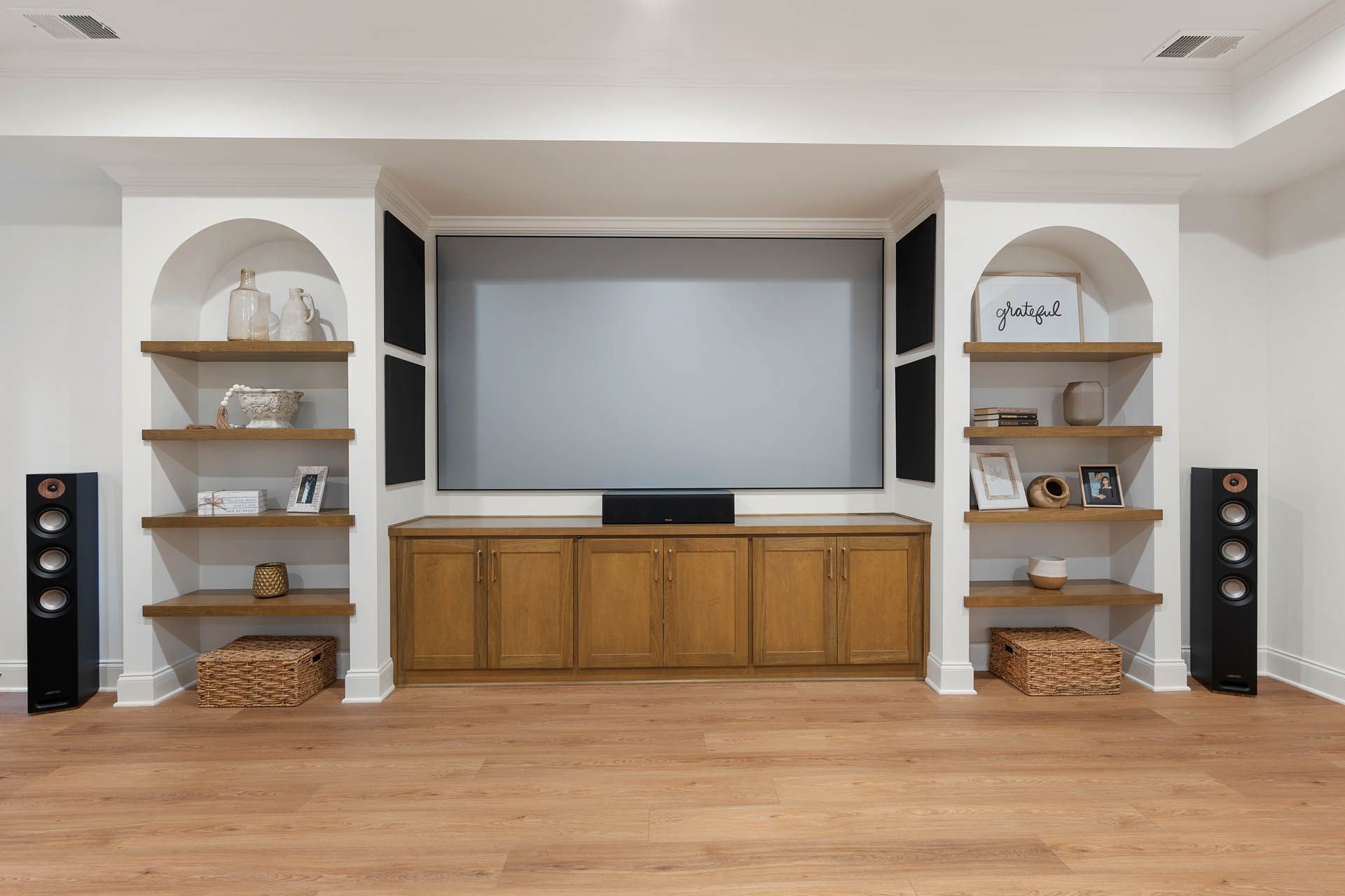 A home entertainment center with a large screen flanked by shelves, speakers, and wooden cabinets against a white backdrop.