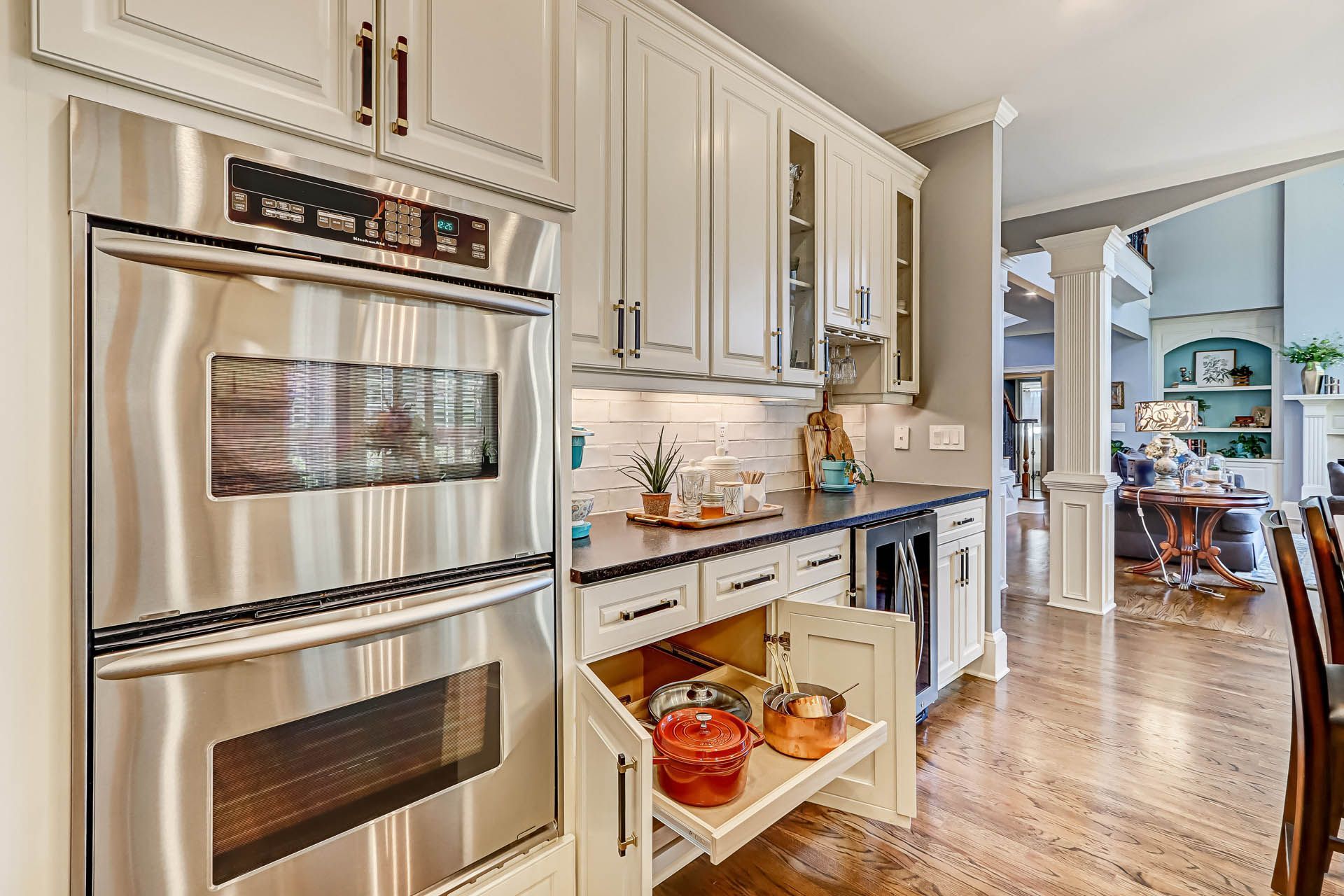 Stainless steel oven and white cabinets in a kitchen. A pull-out drawer reveals storage with red pots. The dining area is visible in the background.