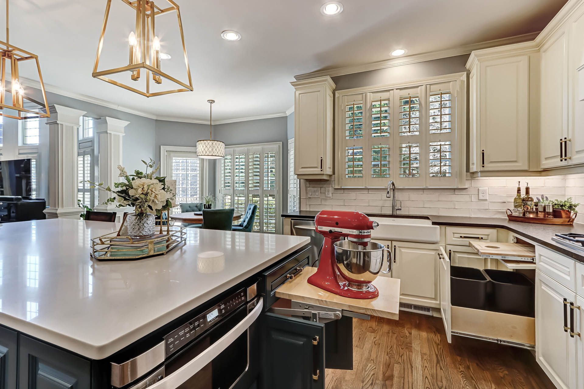 A modern kitchen with white cabinets and a large island, featuring a red stand mixer on a pull-out shelf.