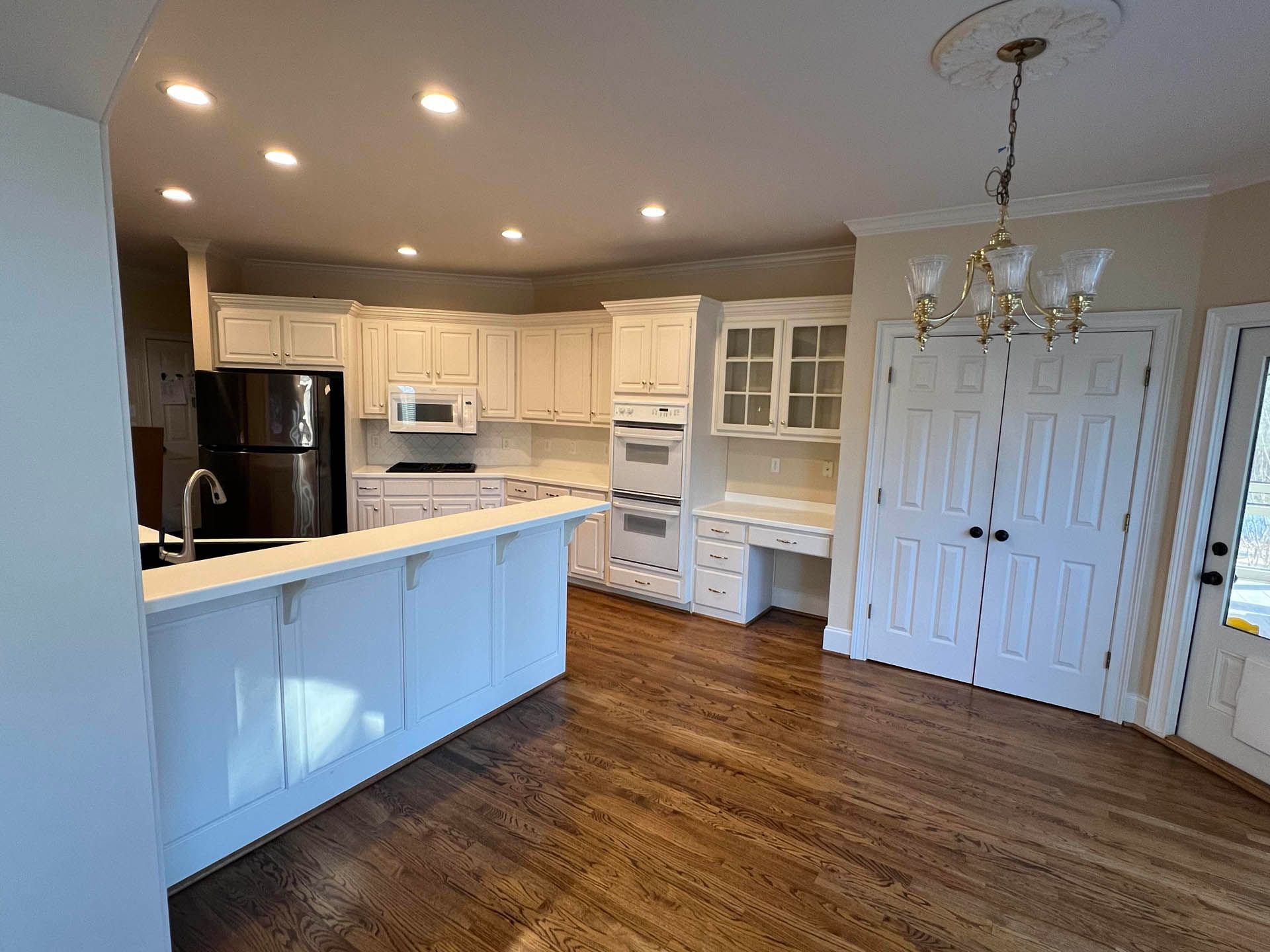 Spacious kitchen with white cabinets, appliances, and a breakfast bar, featuring wooden floors and a chandelier.