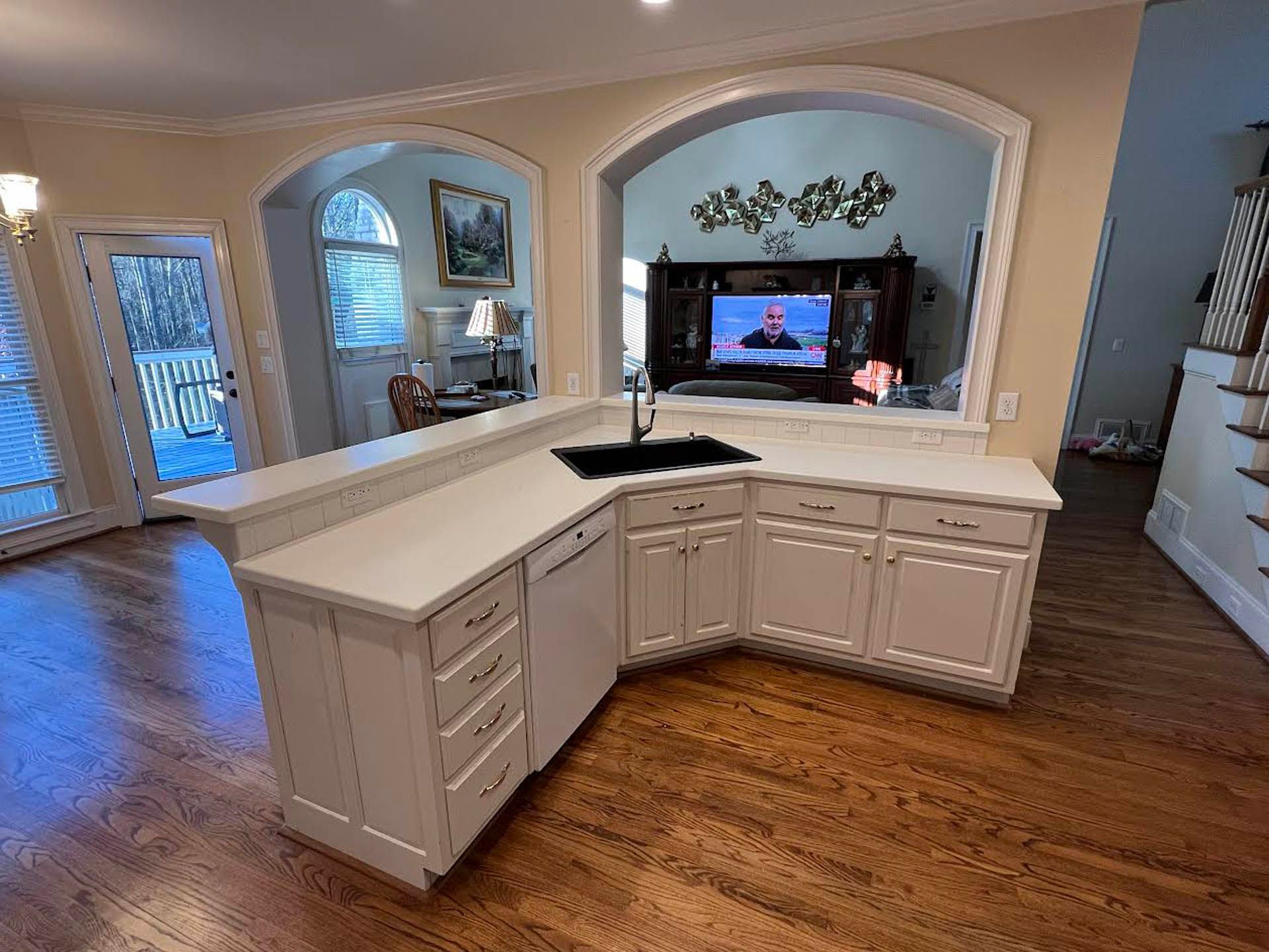A bright kitchen island with a black sink, white cabinets, and countertops. The island is situated on a wood floor.