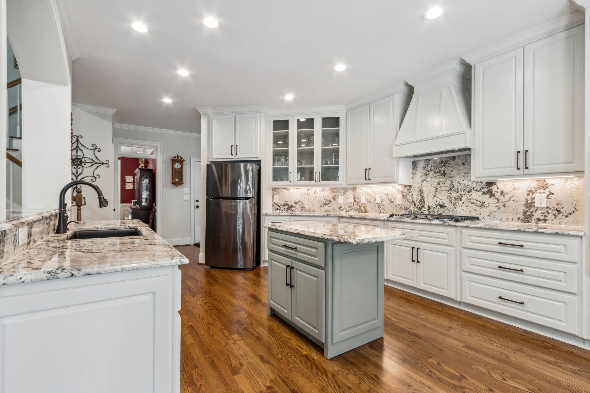 A modern kitchen with white cabinets, granite countertops, stainless steel appliances, and a gray island with hardwood floors.