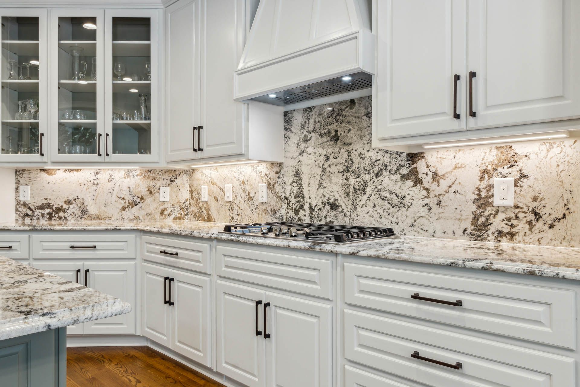 White kitchen with granite countertops, white cabinets, and a brown backsplash.