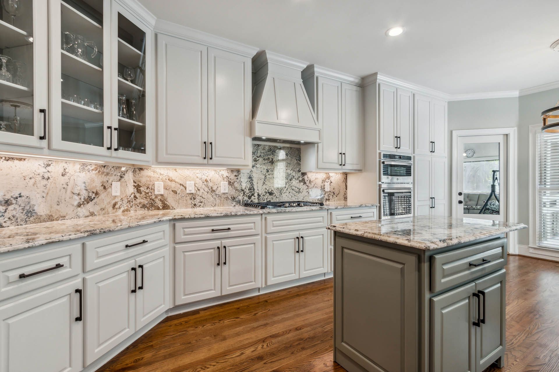 Light gray kitchen with white countertops, dark wood floors, and a gray island. Cabinets have black hardware.