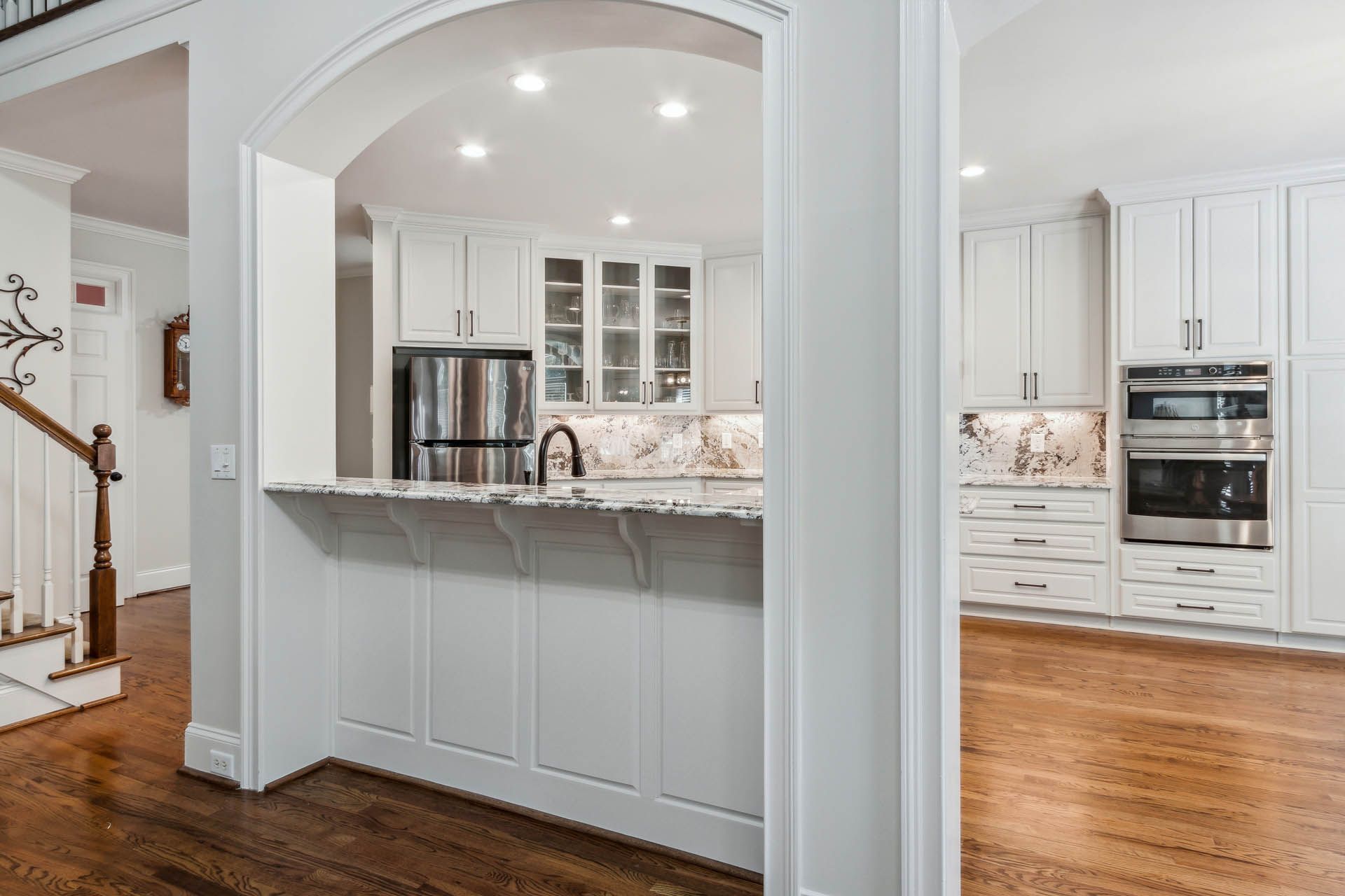 White kitchen with archway leading to a breakfast bar, hardwood floors, and built-in oven.