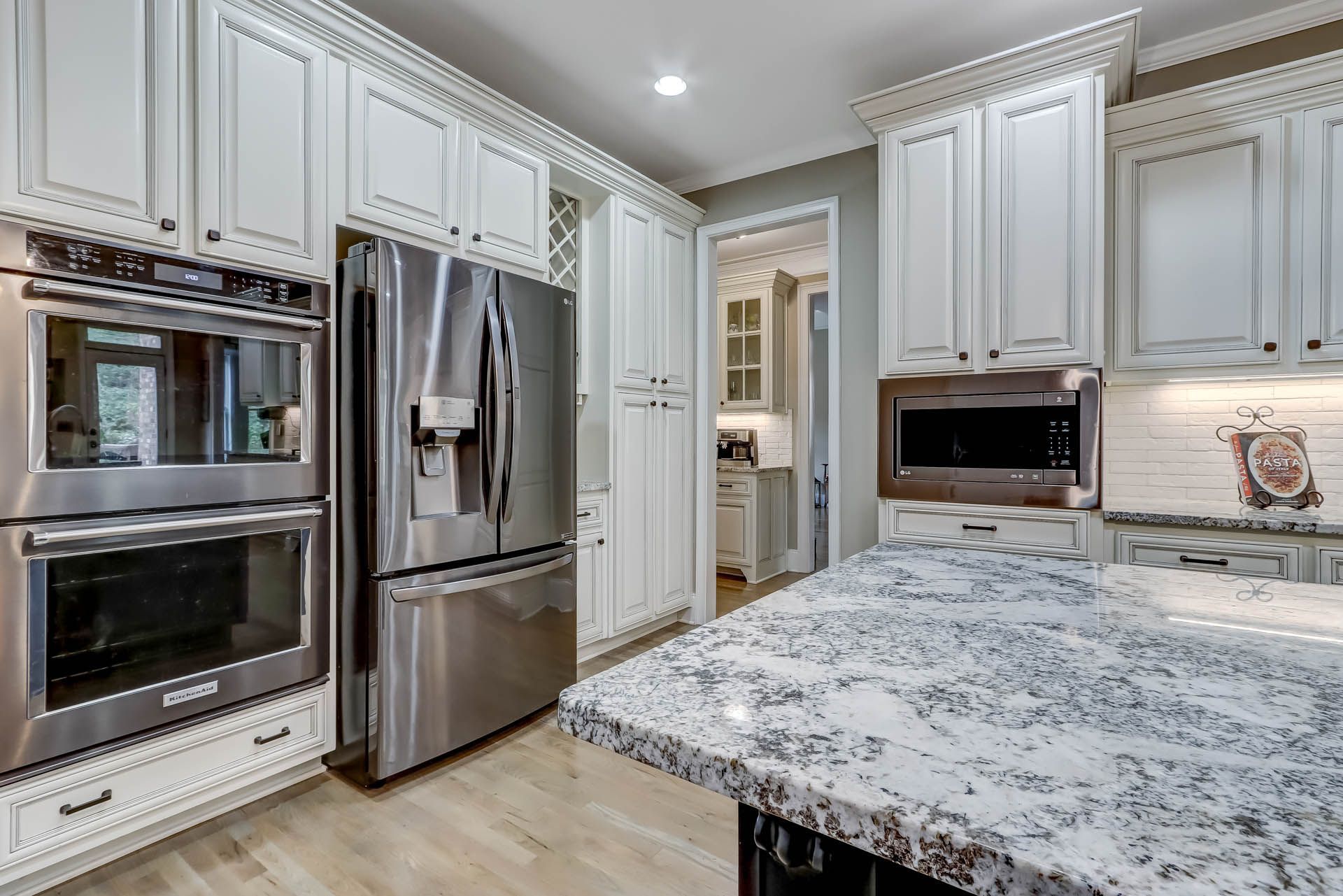 White kitchen with stainless steel appliances, granite countertop, and doorway to another room.